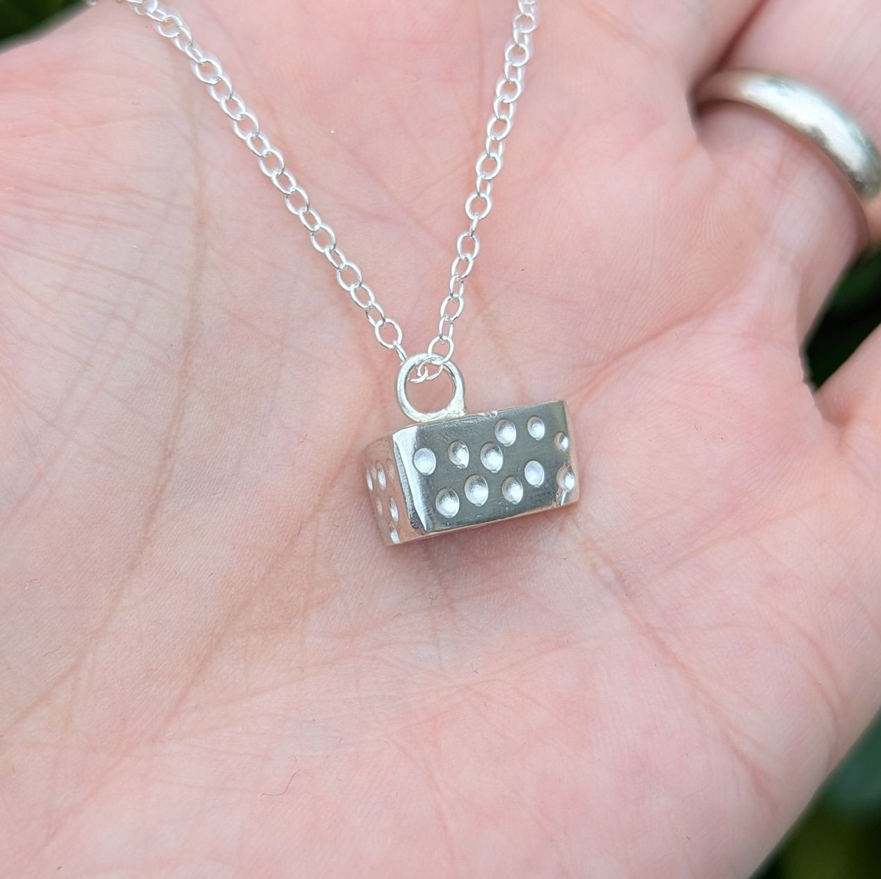 Side profile of a sterling silver cheese necklace resting in a palm of a hand