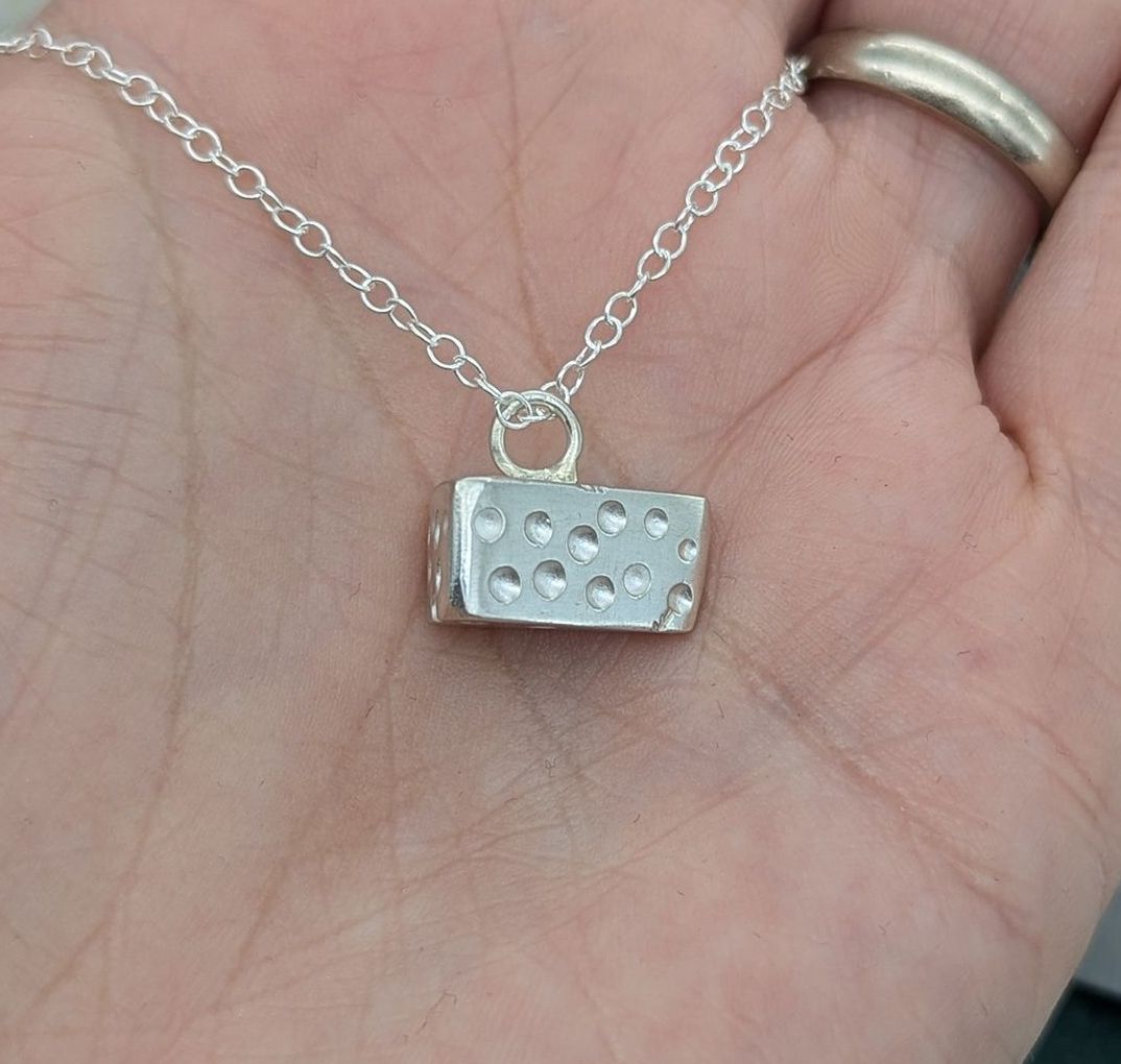 A sterling silver cheese shaped necklace resting on a palm of the hand