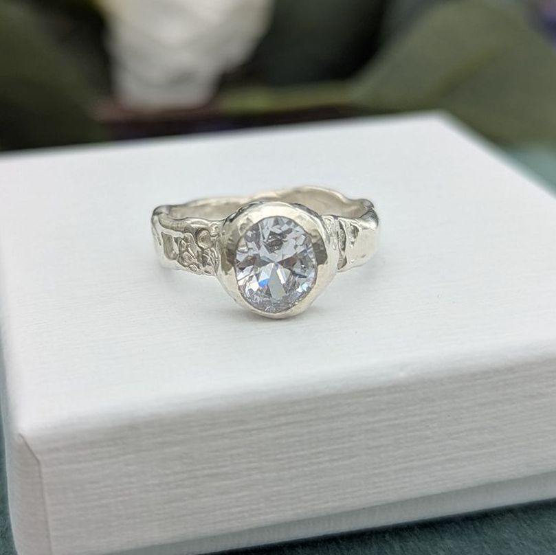 A silver CZ facet gem set ring resting on a white jewellery box