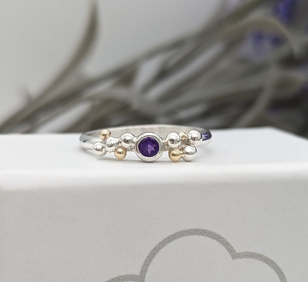 A silver & amethyst with gold granulation ring resting on a white jewellery box