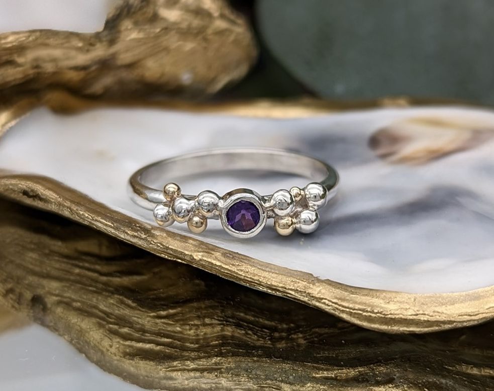 A silver & gold granulation ring with an amethyst gemstone resting on a gold gilded oyster shell