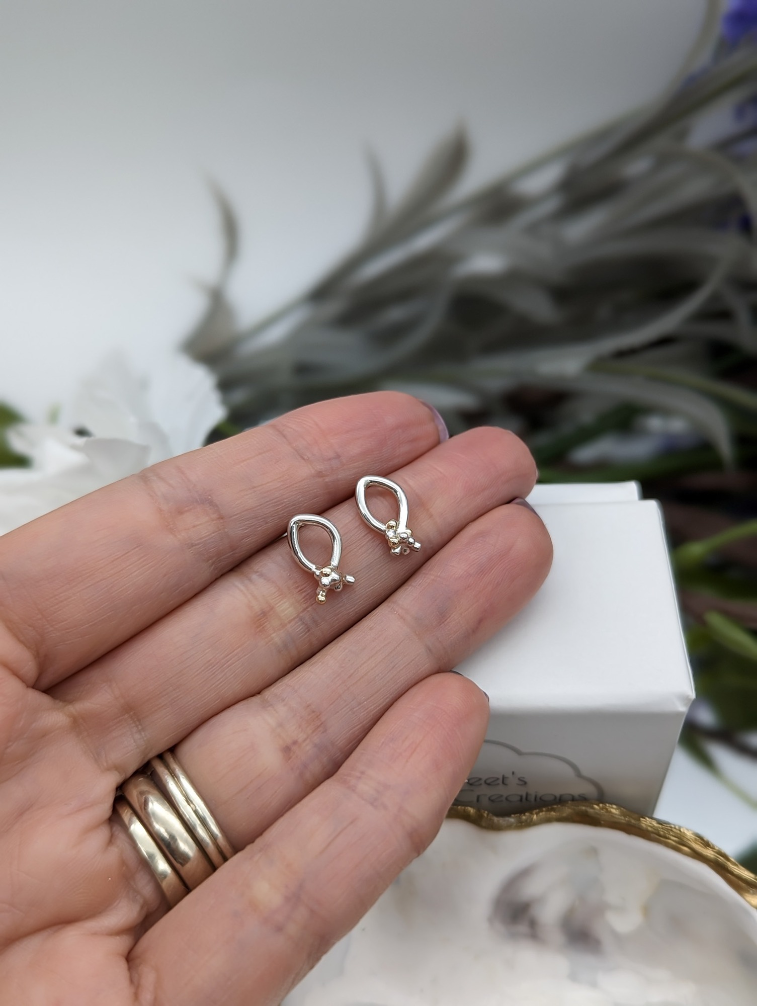 Silver & gold granulation stud backed earrings held in a hand 