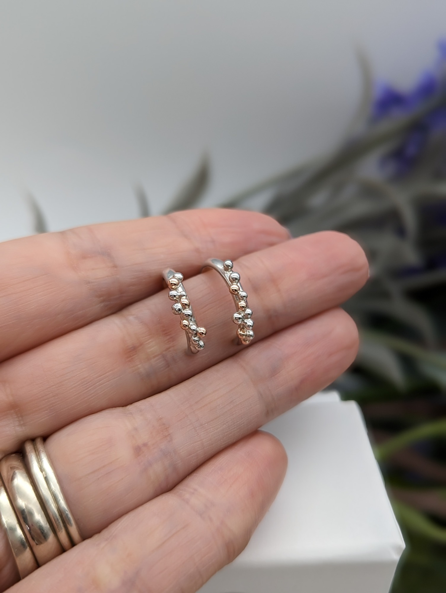Silver & rose gold half hoop earrings being held on a hand