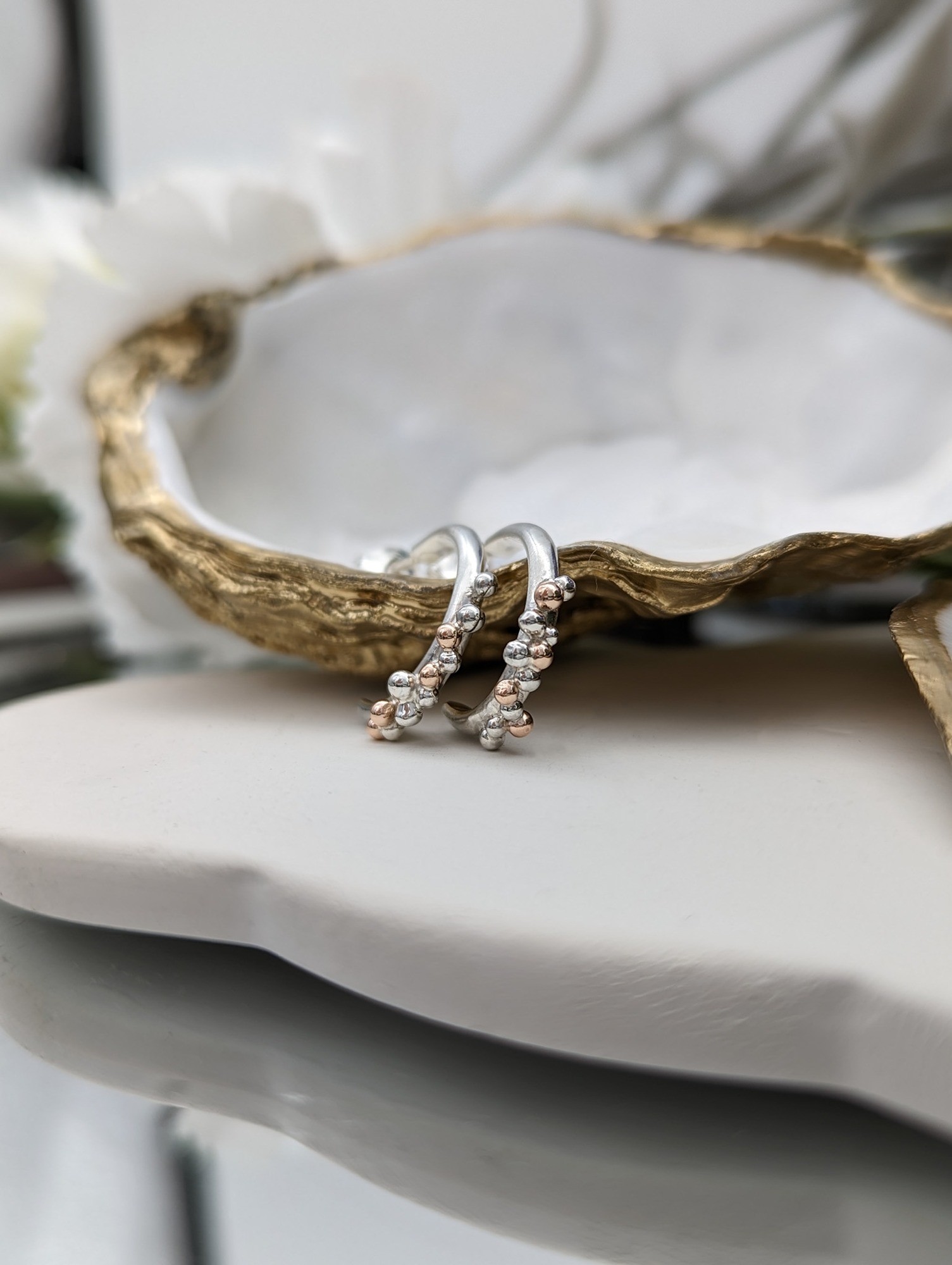 Silver & rose gold half hoop earrings resting on a gold gilded oyster shell