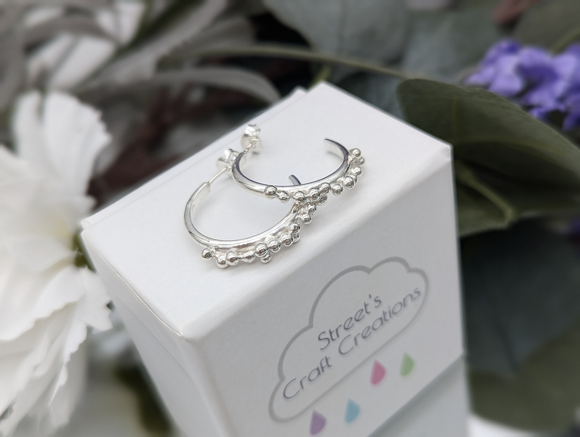 Silver granulation stud baked half hoops resting on a white jewellery box