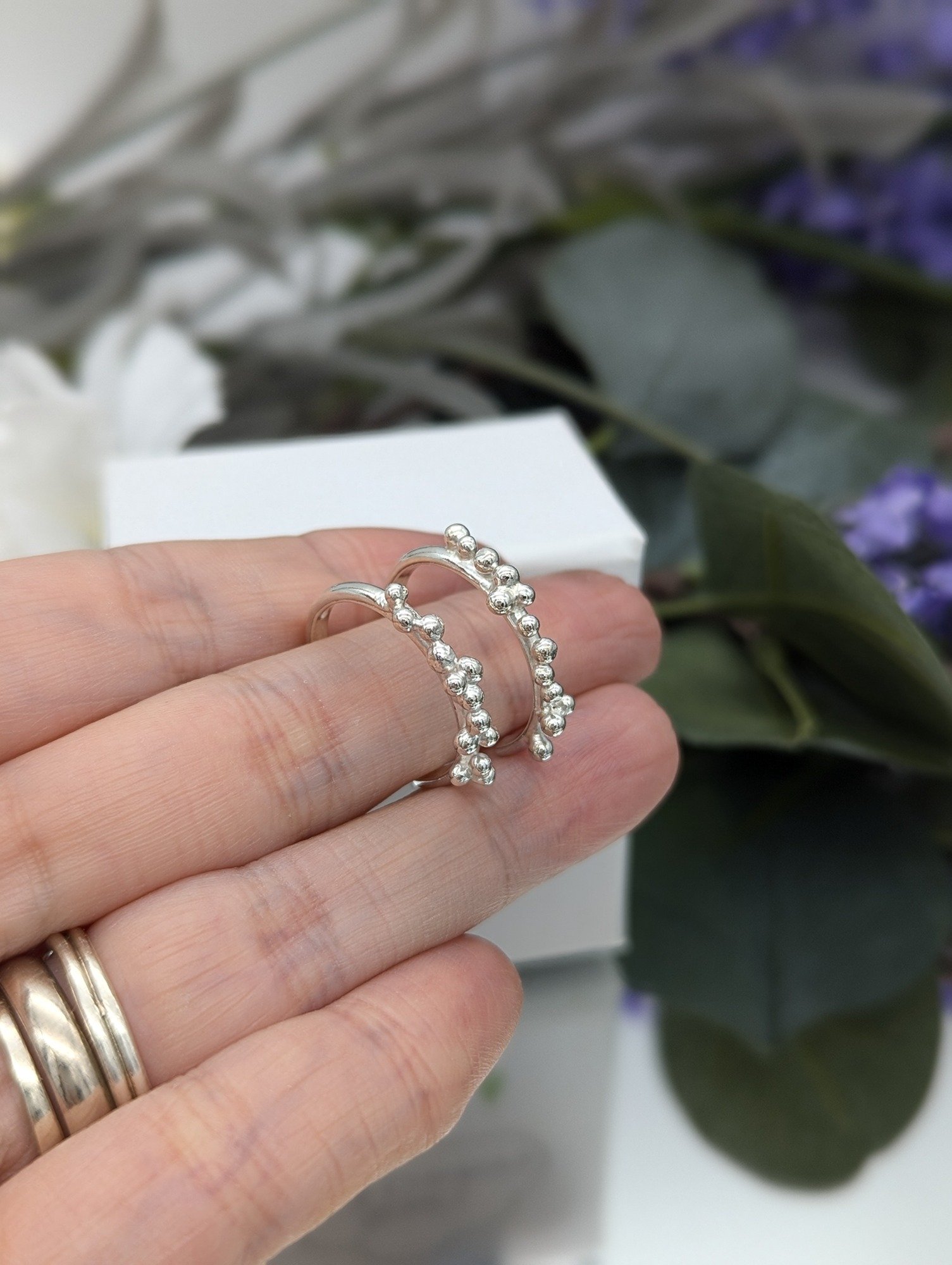 Silver granulation half hoop earrings resting on a hand