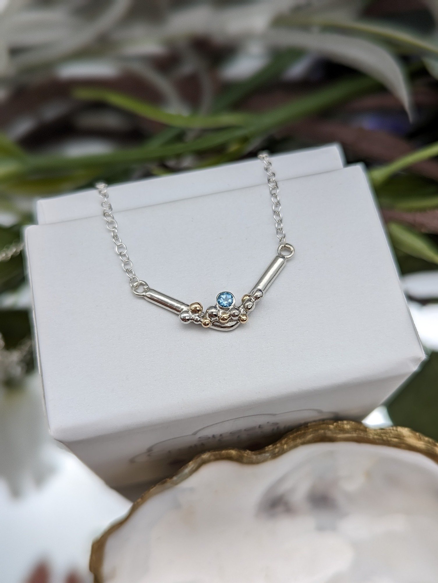 Swiss blue topaz gemstone necklace with silver & gold granulation resting on a white jewellery box
