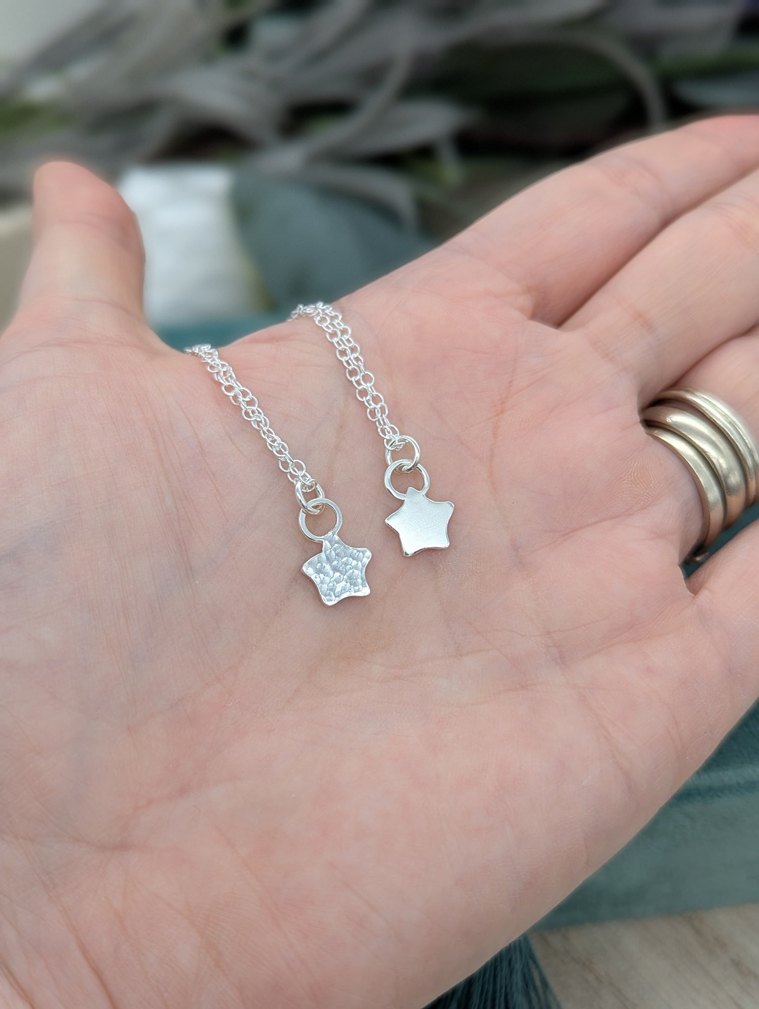 2 silver star necklaces being held in a hand