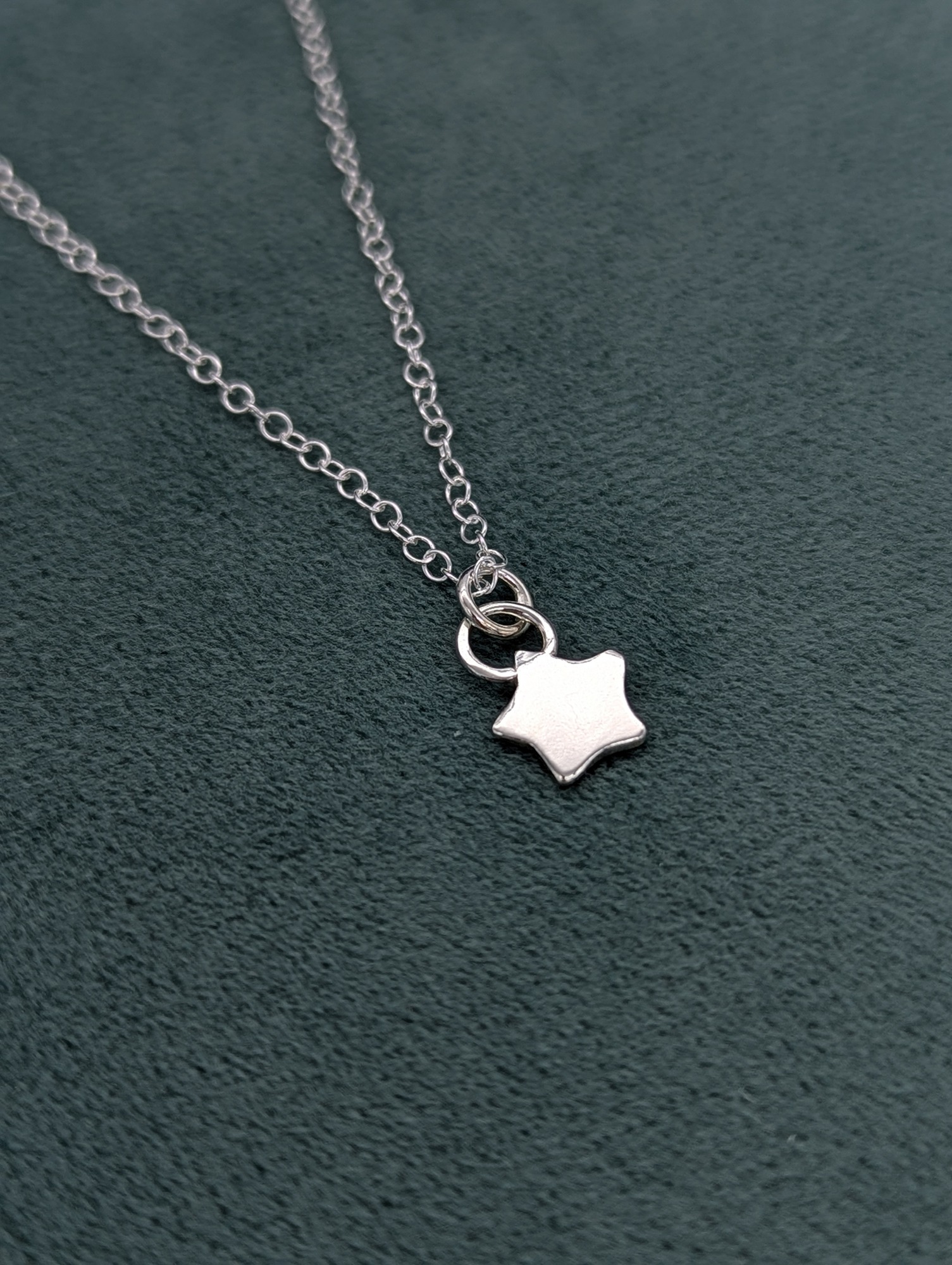 Shiny silver star necklace on a teal fabric jewellery box