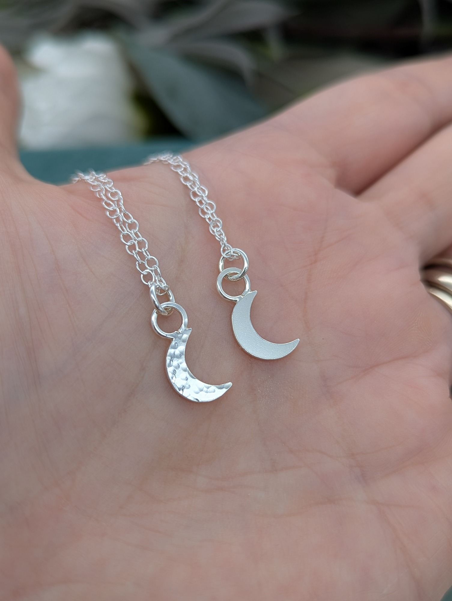 2 silver crescent moon necklaces with different finishes, resting on a hand