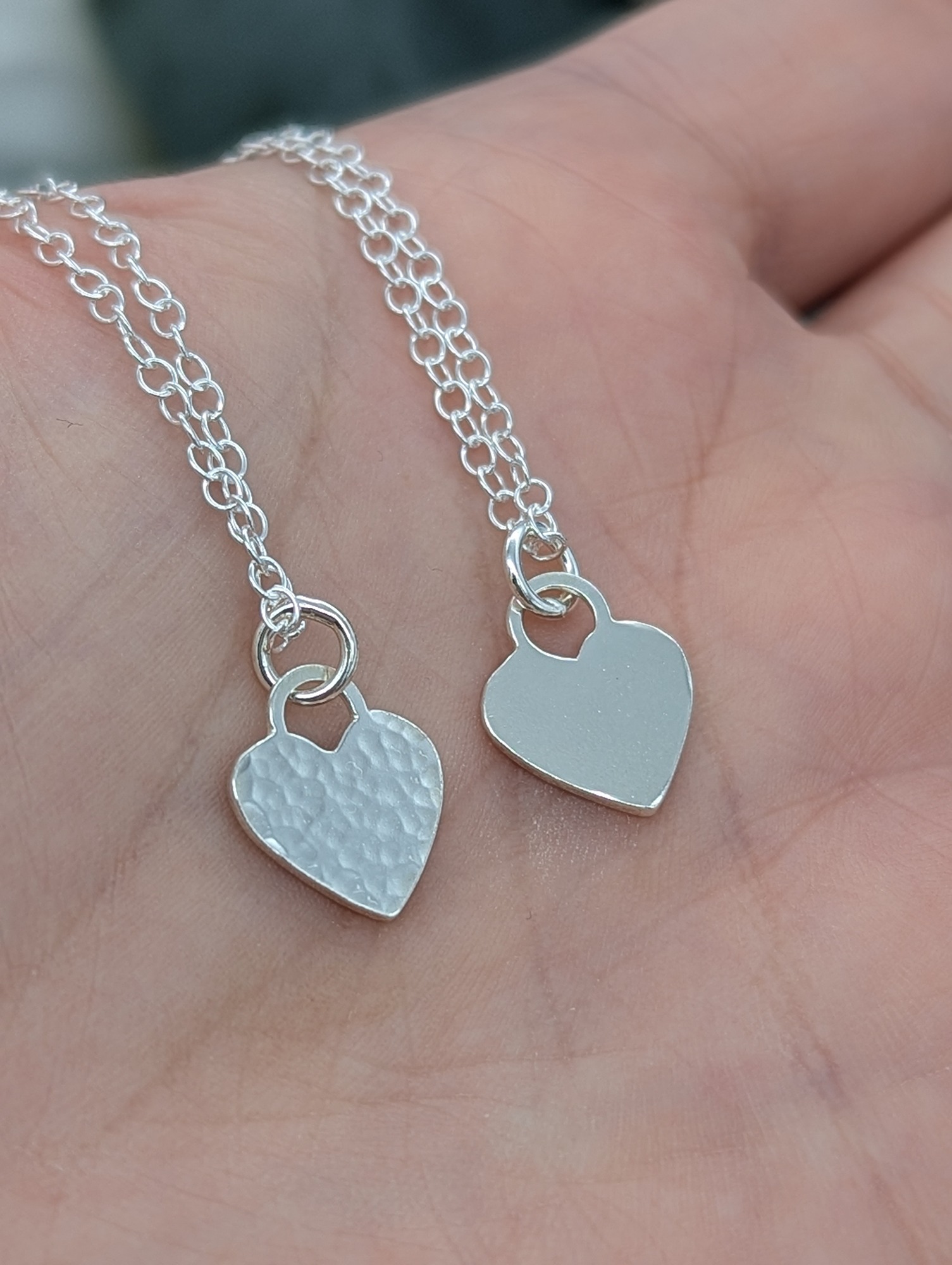 Sterling silver heart necklaces one textured one high polish resting on a hand