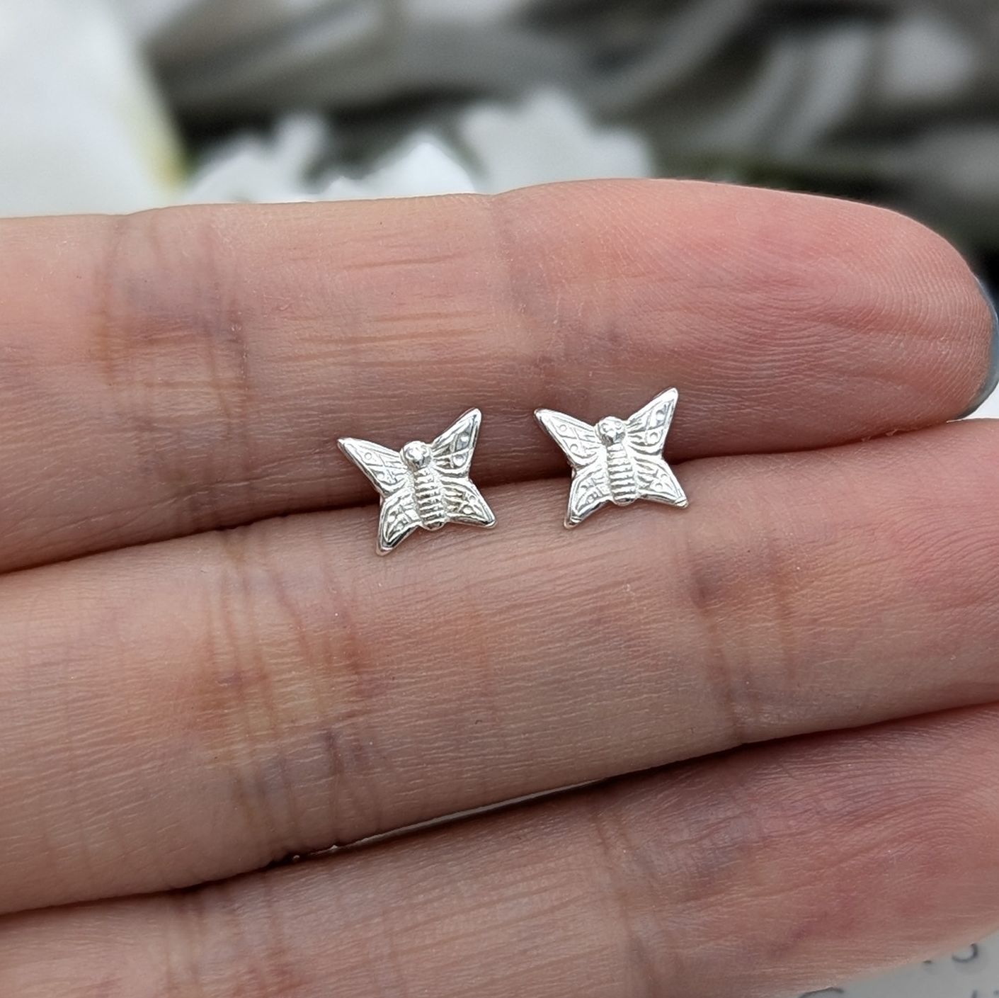 Silver butterfly stud earrings in a hand