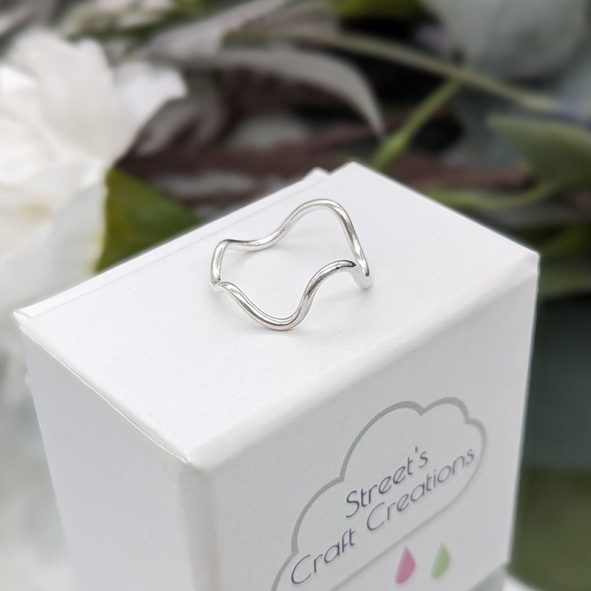 silver deep wave ring on a whire box with a leafy background