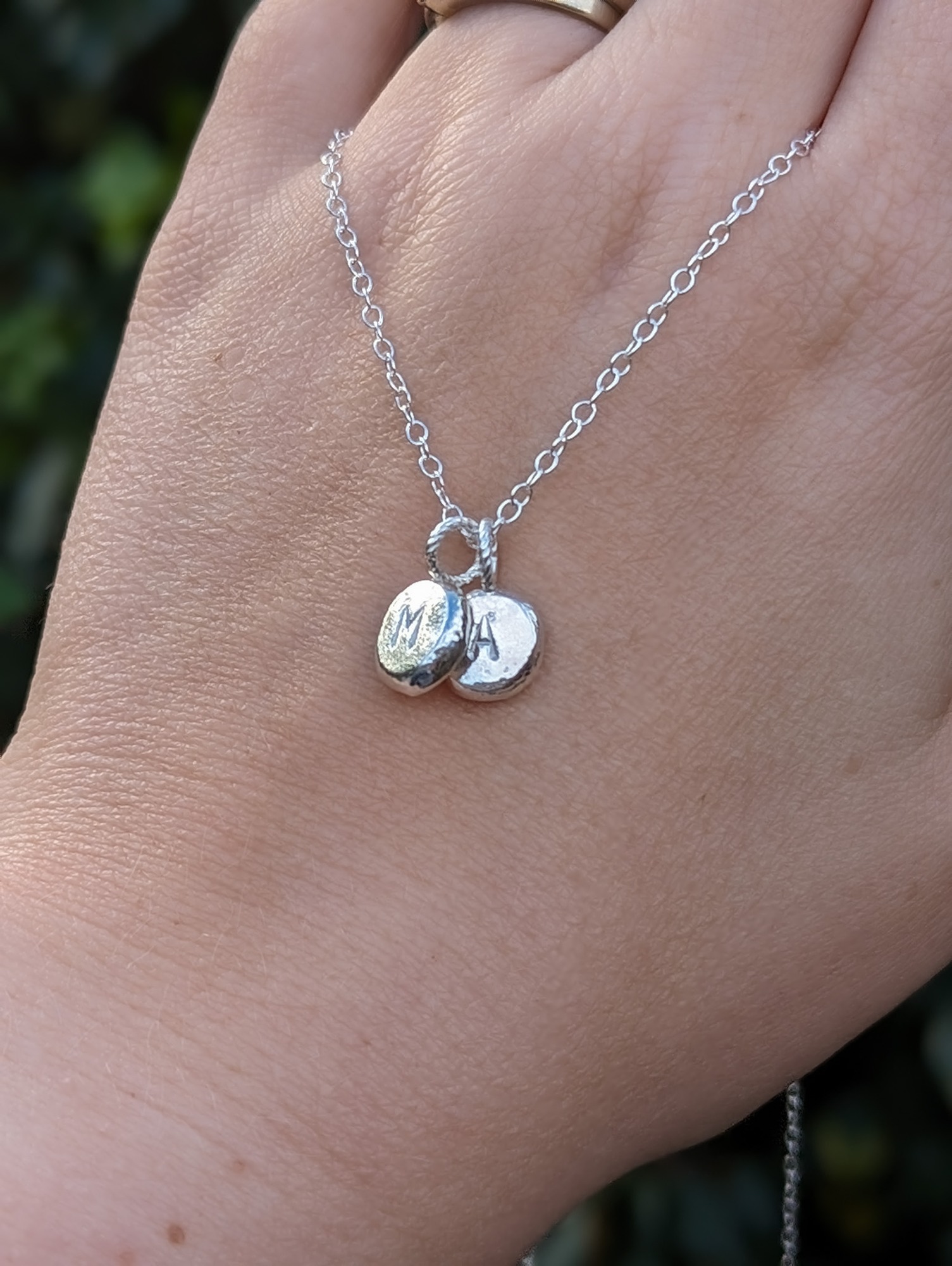 Silver initial pebble necklace with the initials M, A modelled on a hand