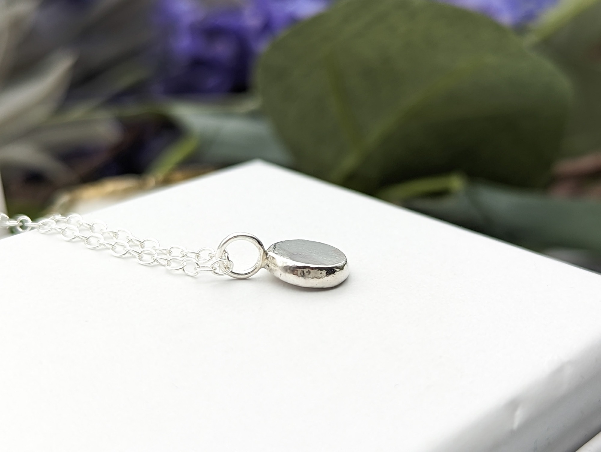 Side profile of silver droplet necklace on white jewellery box