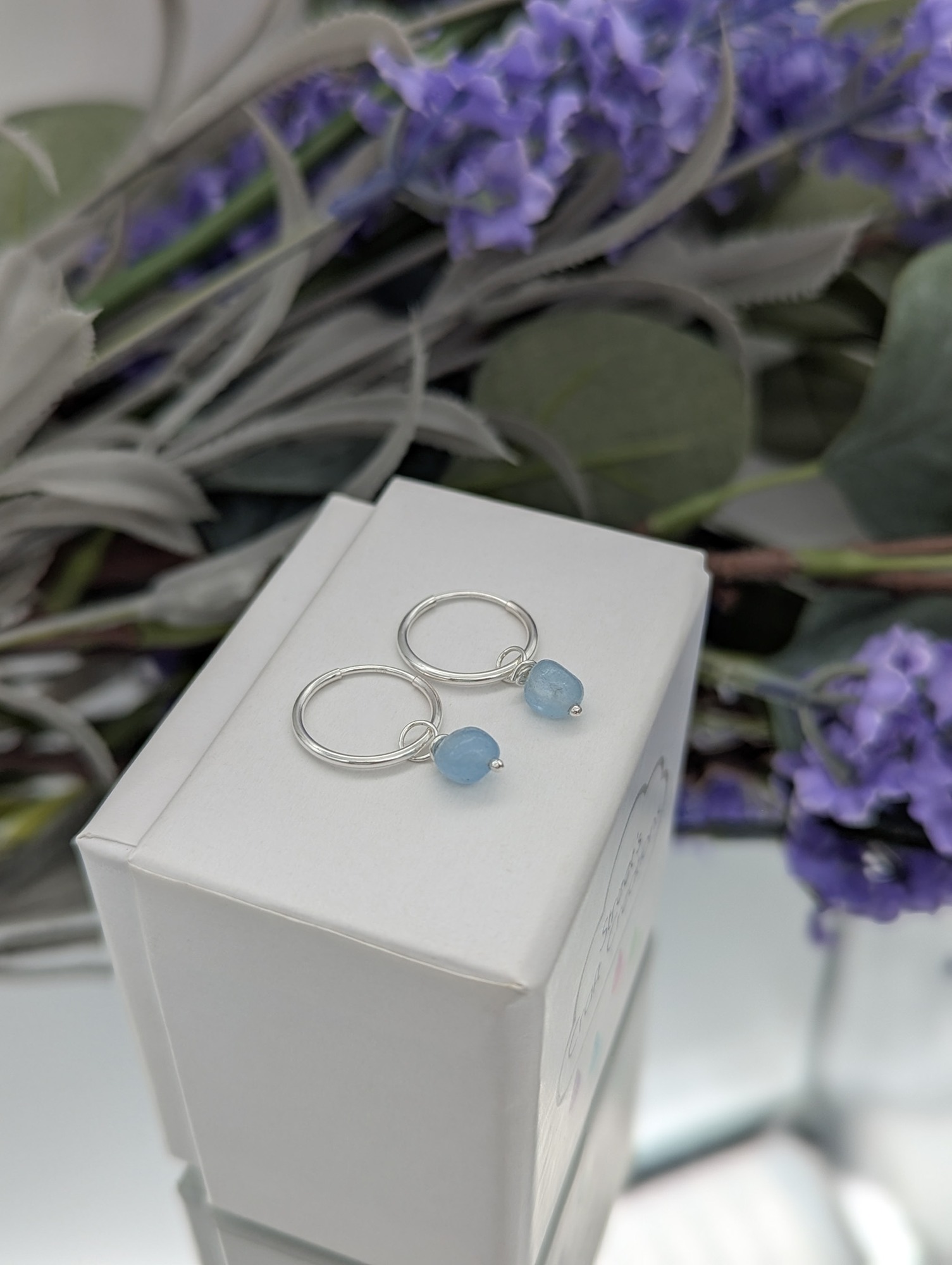 Aquamarine hoop drop earrings resting on a white jewellery box