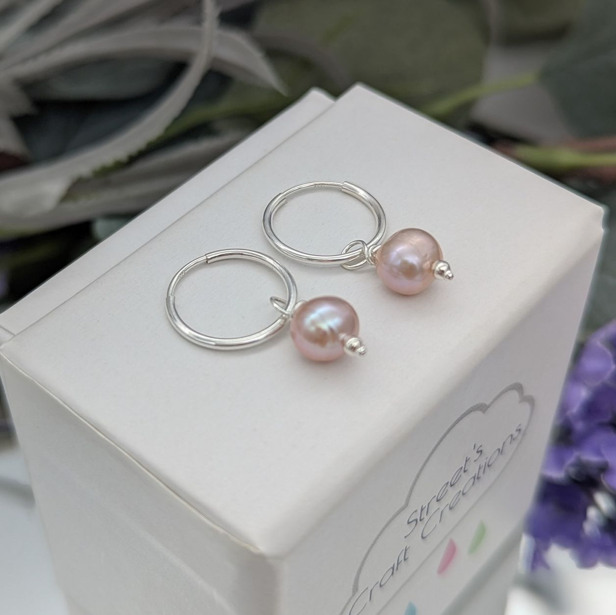 Pink pearl and silver hoop drop earrings on a white jewellery box