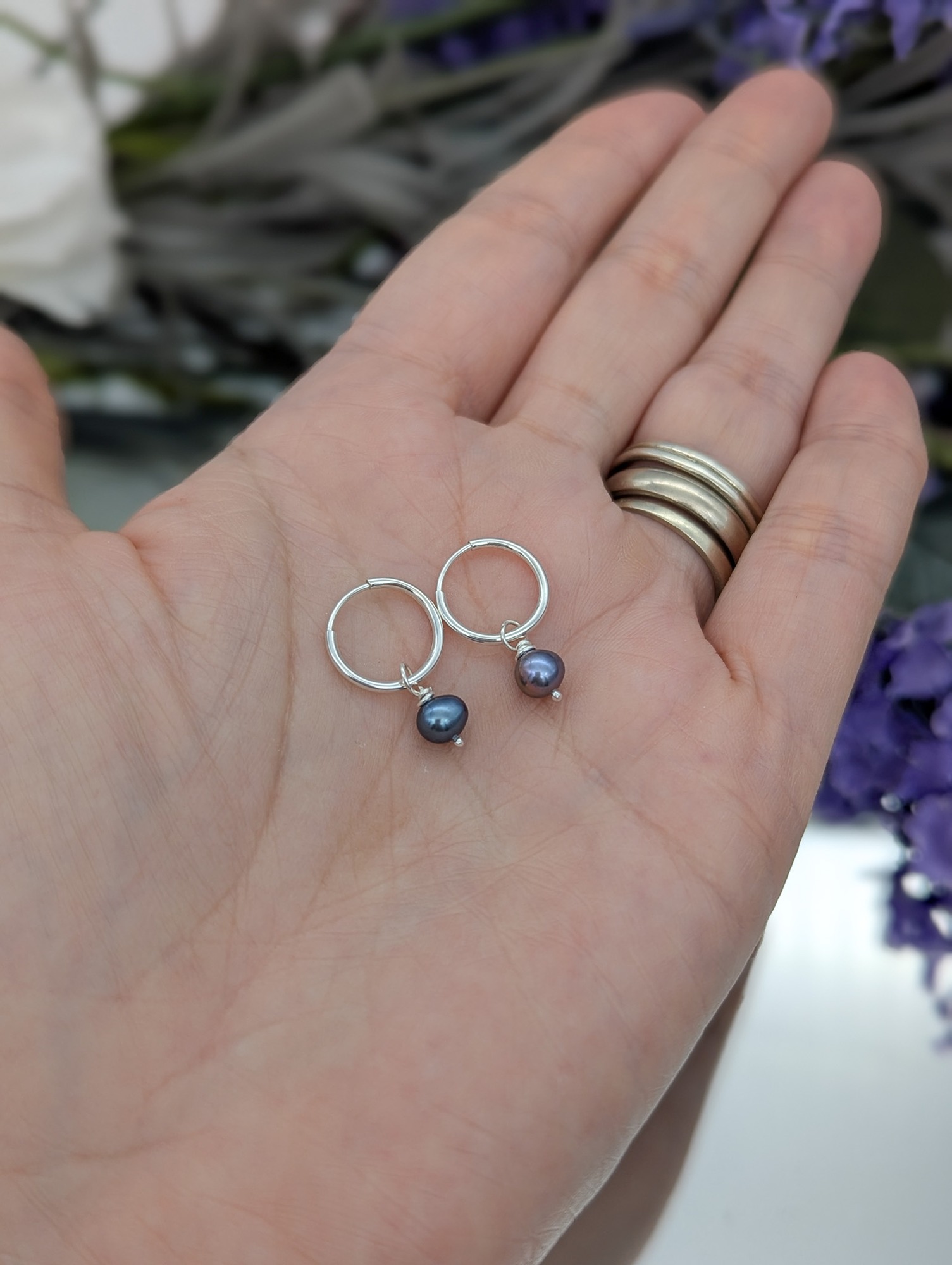 Peacock pearl and silver hoop earrings on a hand
