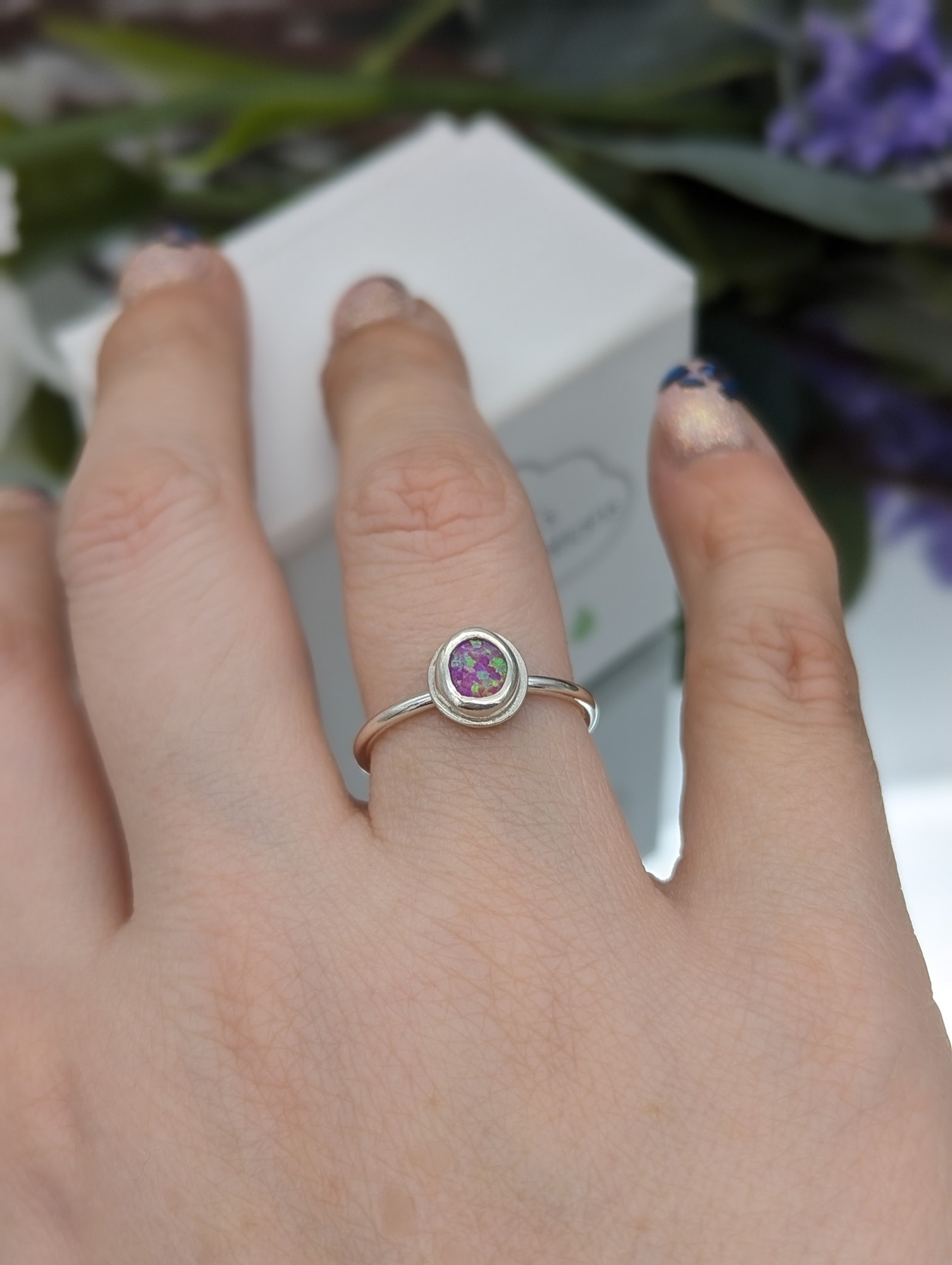 Pink created opal and silver ring being worn on a hand