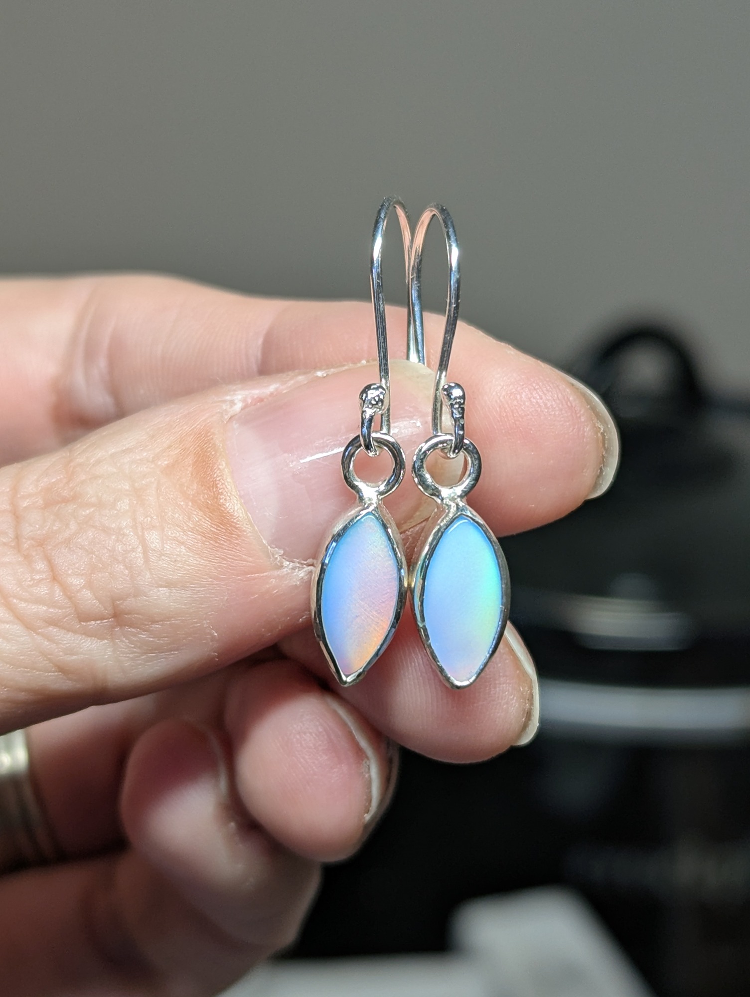 Aurora opal silver drop earrings being held in a hand 