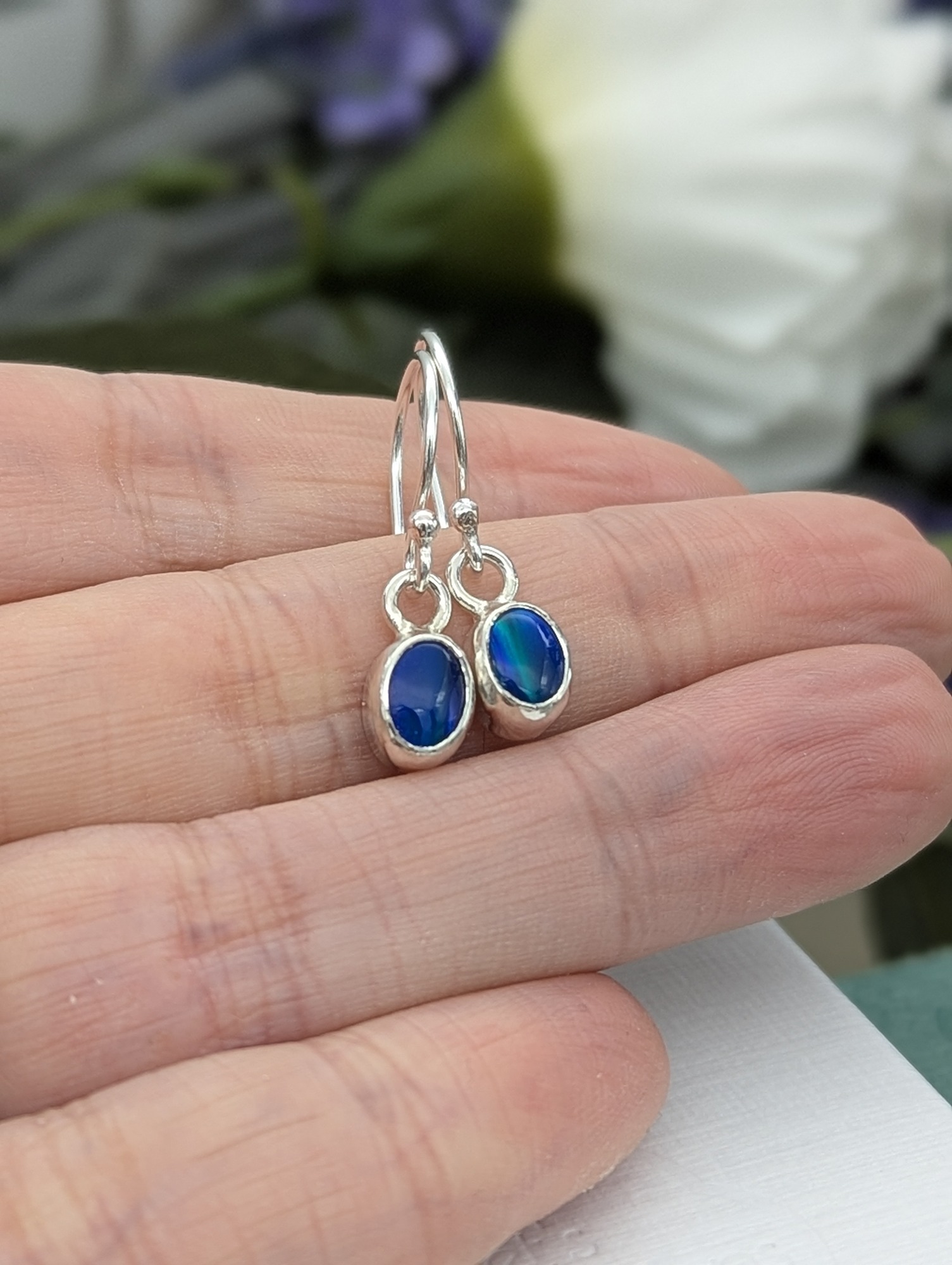 Ocean blue aurora opal earrings held in a hand