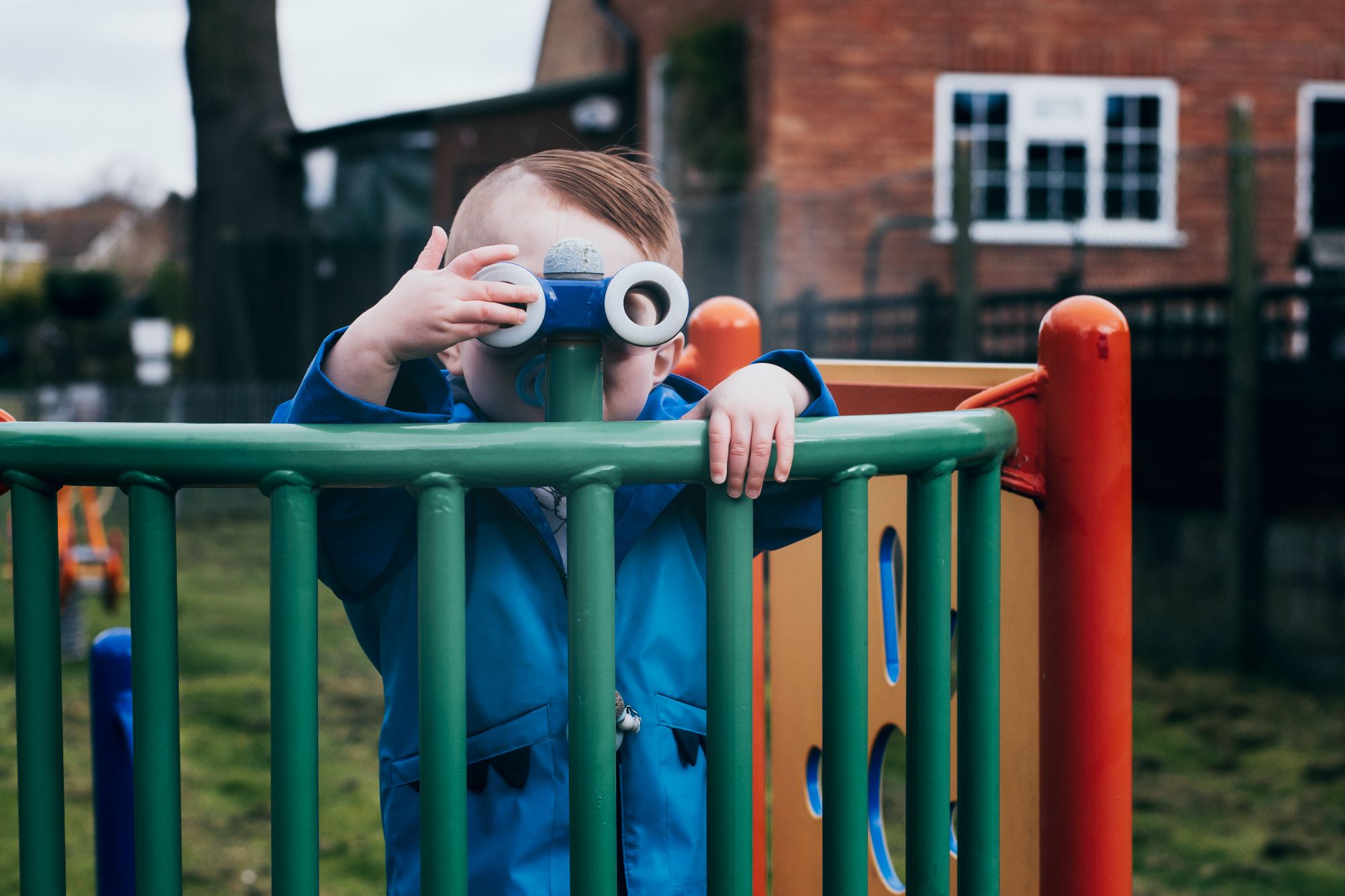 A little boy looks through some binoculars at the park,