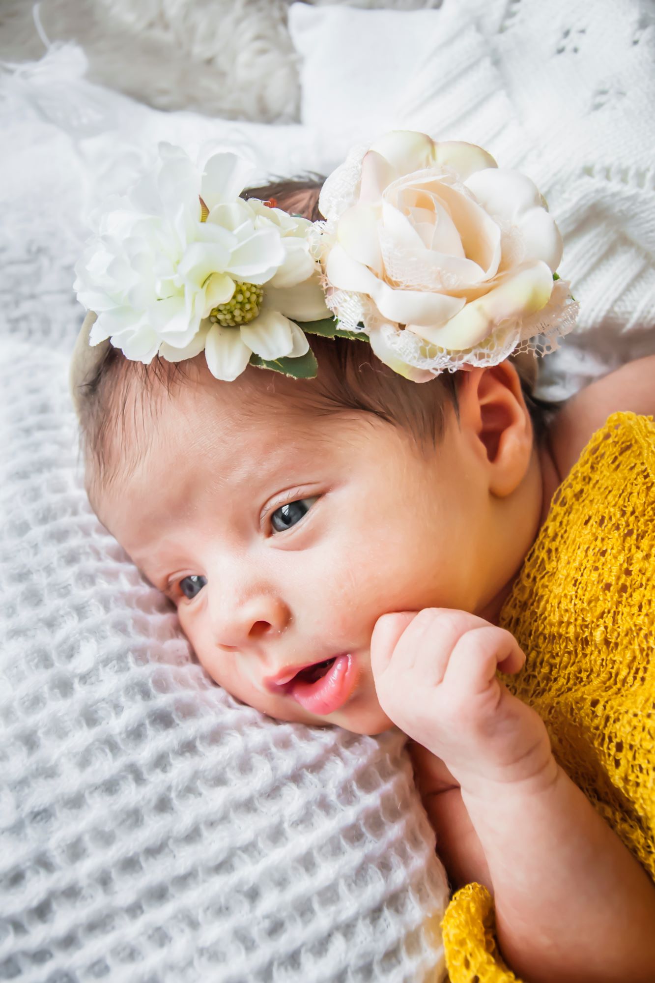 Newborn baby lays in her cot with flowers on her head at a north yorkshire at home newborn photoshoot