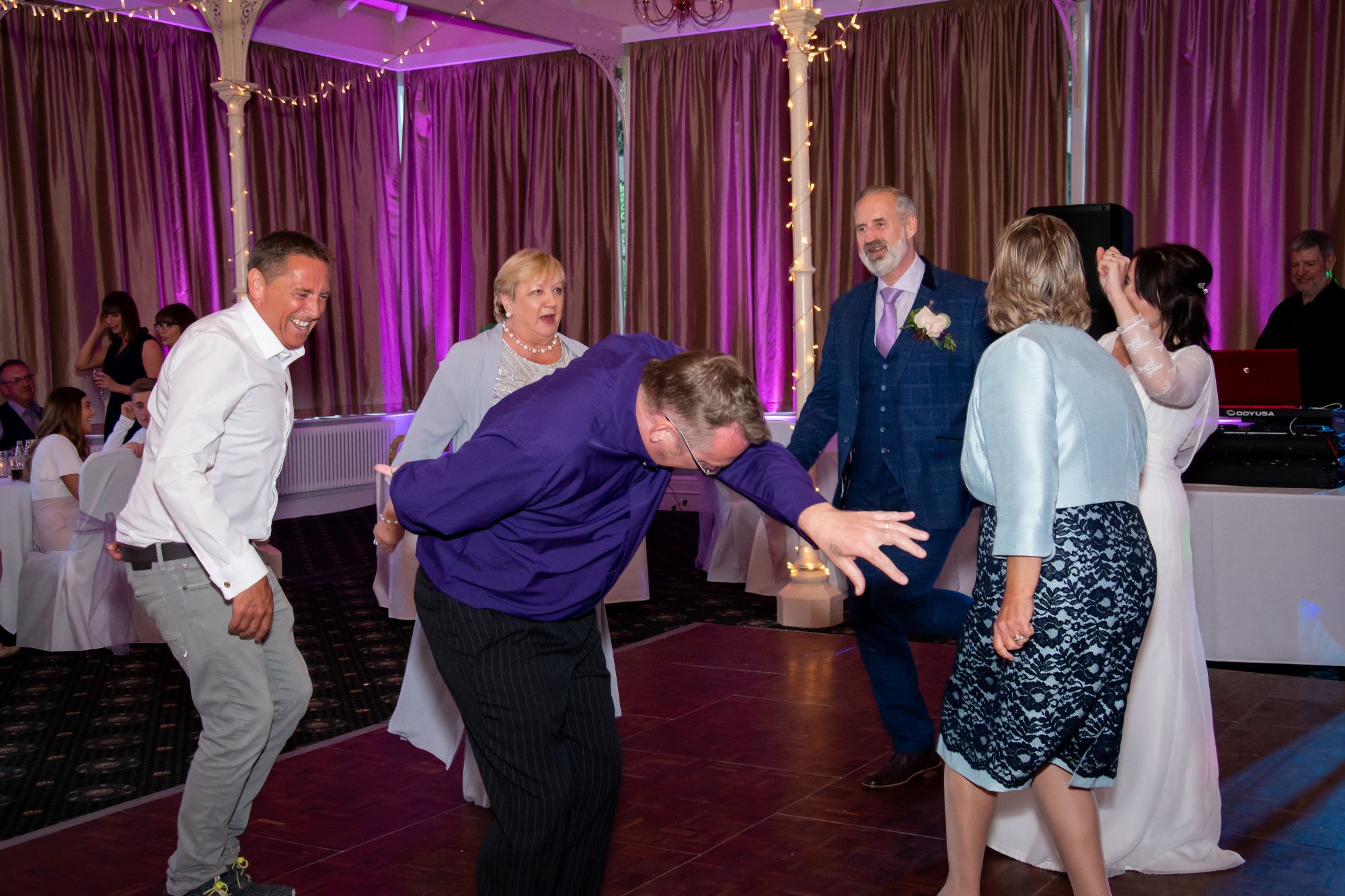 The bride and groom dance along with guests as one man pretends he's an elephant.