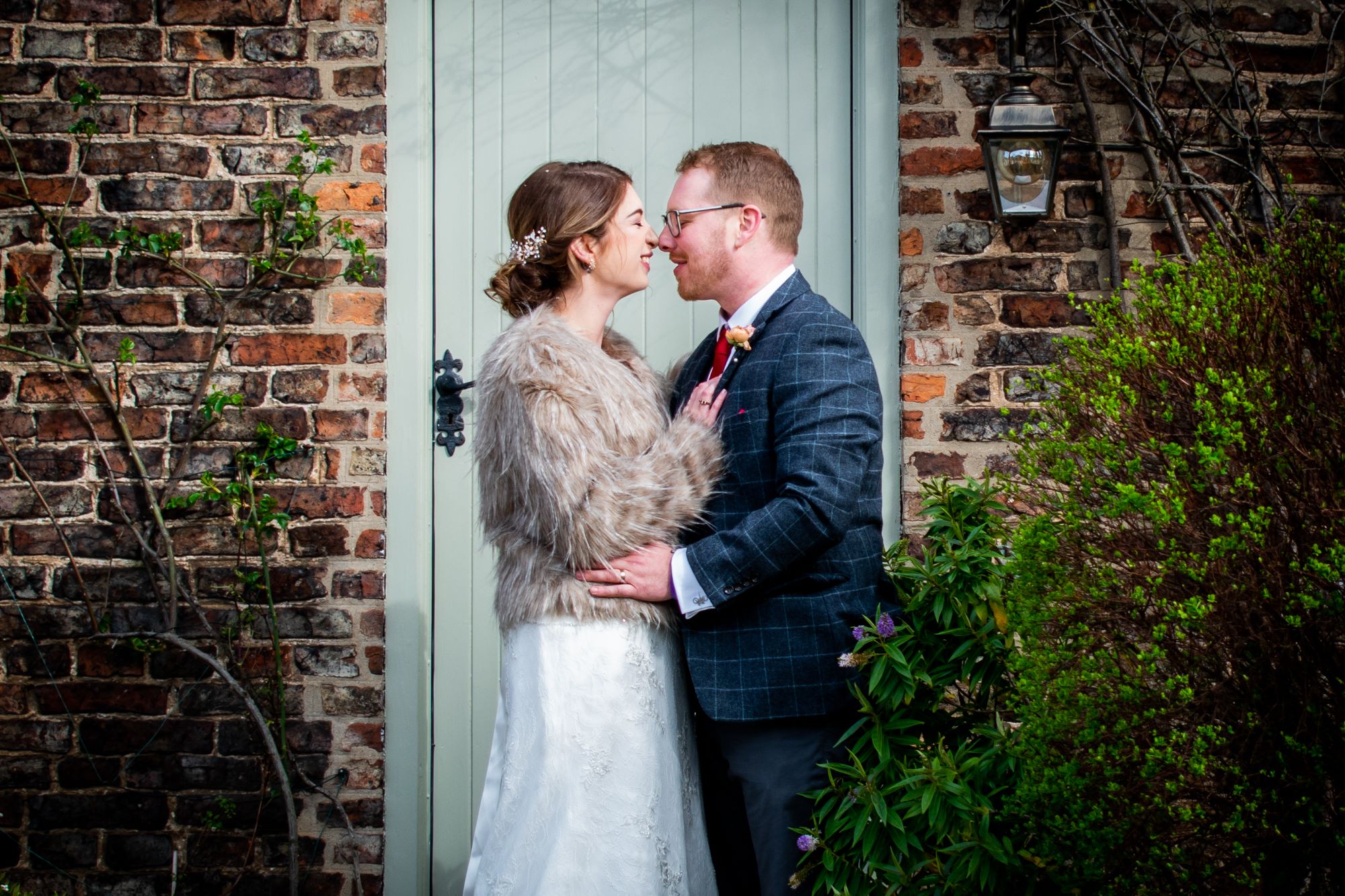 the bride and groom touch noses as they embrace infront of a cottage door.