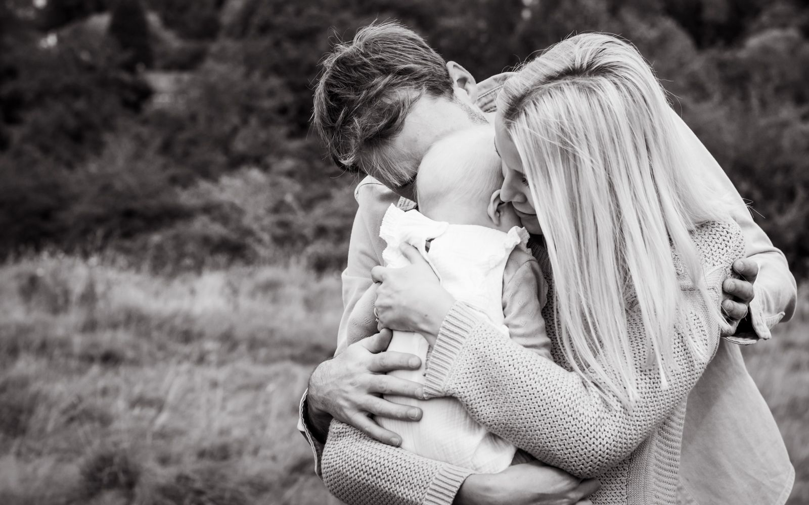 Mum and dad hug their little girl to comfort her during their baby photoshoot in the countryside