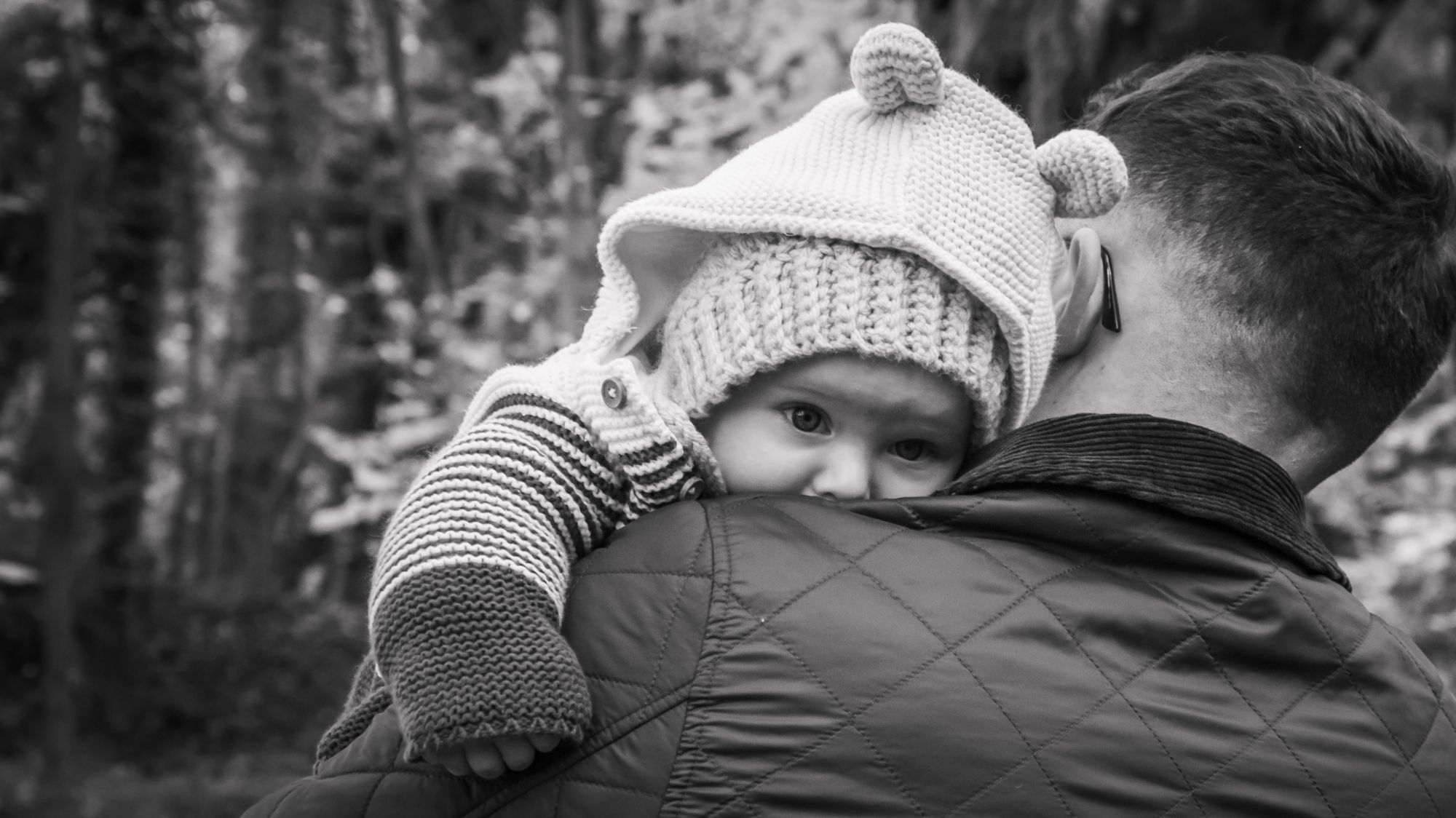 A baby peers over his Dad's shoulder as they walk through Pickering Woods on their Baby Photoshoot