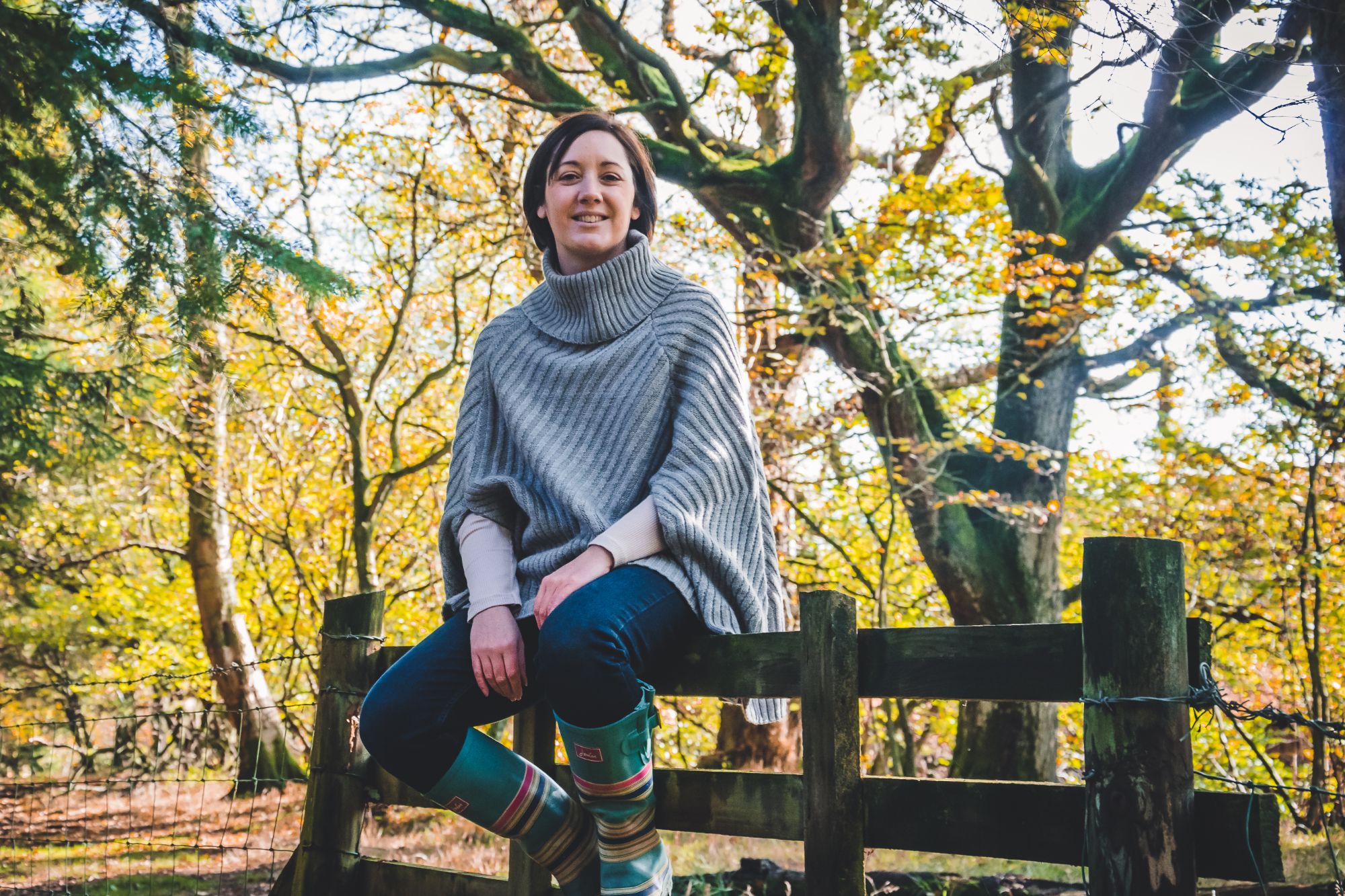Empowering Photography for women in North Yorkshire. A woman sits on a fence and smiles while looking directly into the camera lens. She wears her normal clothes and looks beautiful