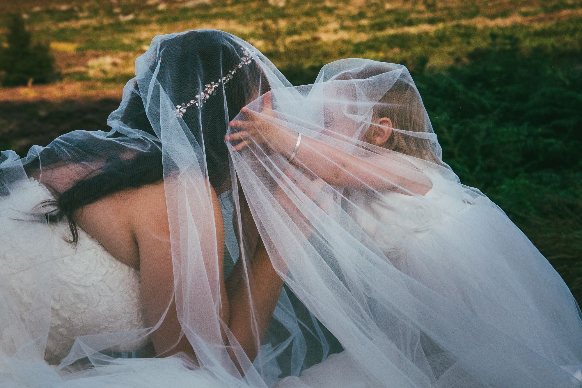 A bride crouches down under her veil and her daughter who's 4 years old has rushed under and is giving her a kiss.