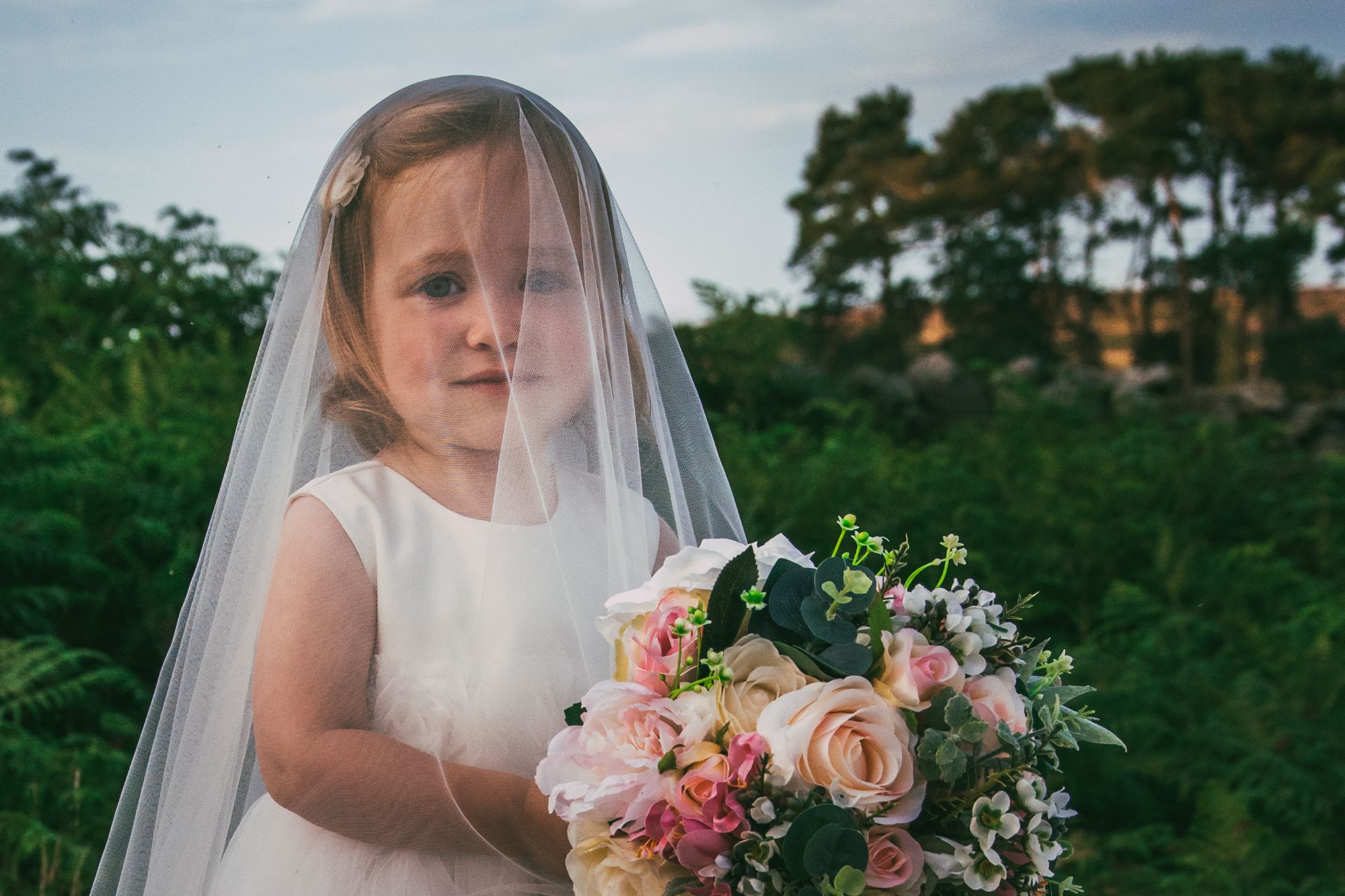 A little girl stands under her mum's veil and holds her bouquet.