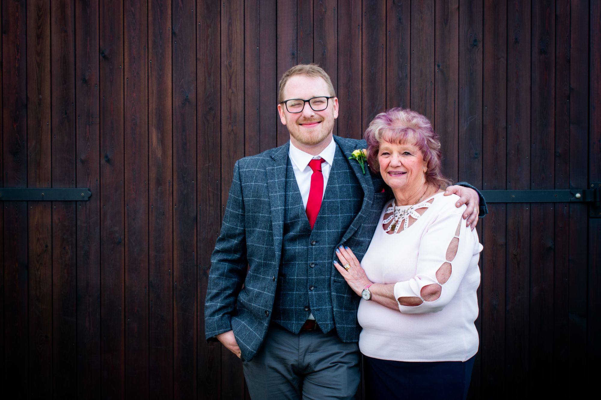 A proud Mum stands with her son, the groom, in front of old barn doors at his wedding in York