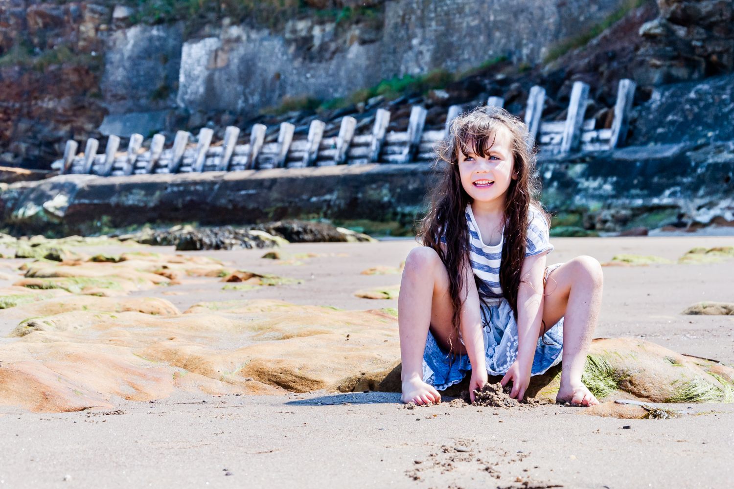 A young girl sits on the beach and looks longingly at the sea