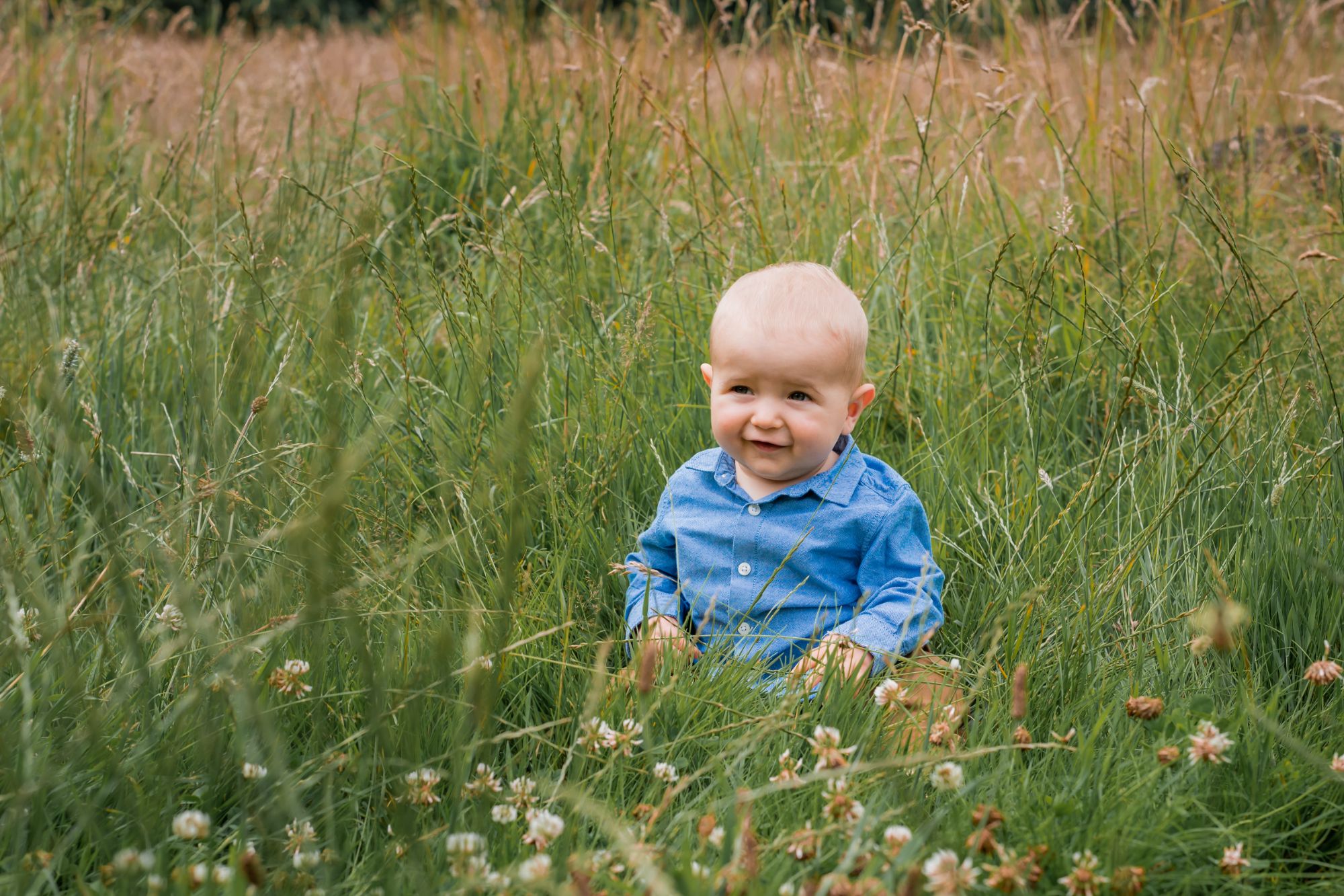 A baby sits in a grass meadow.