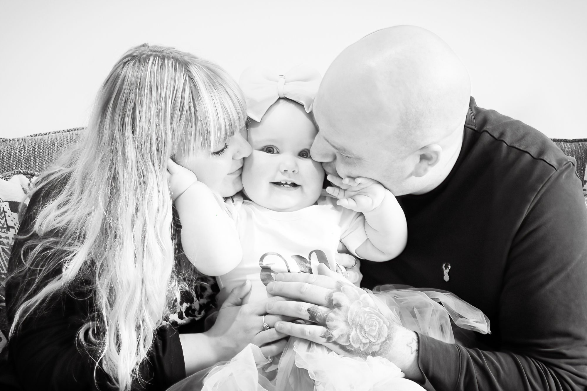 A proud Mum and Dad cuddle and kiss their daughter on her cheeks as they celebrate her first birthday at home