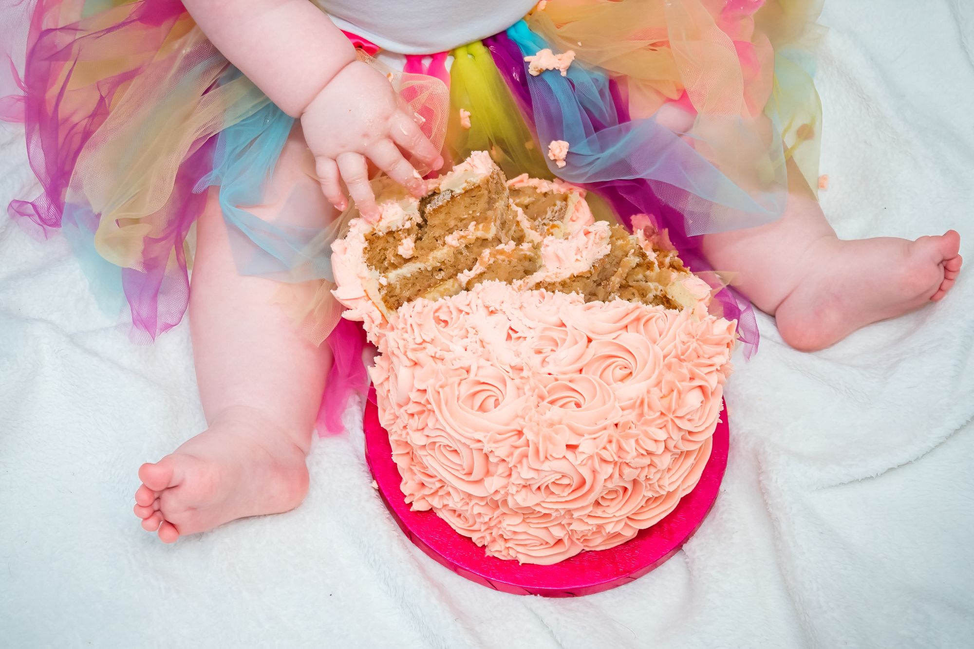 A little girl sits with her birthday cake between her legs and has just pulled off a large chunk ready to eat