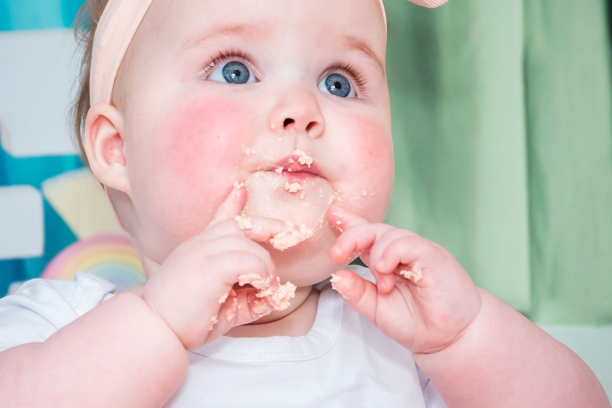 A close up of a little girl's face at her cake smash session. She has icing on her lips and fingers