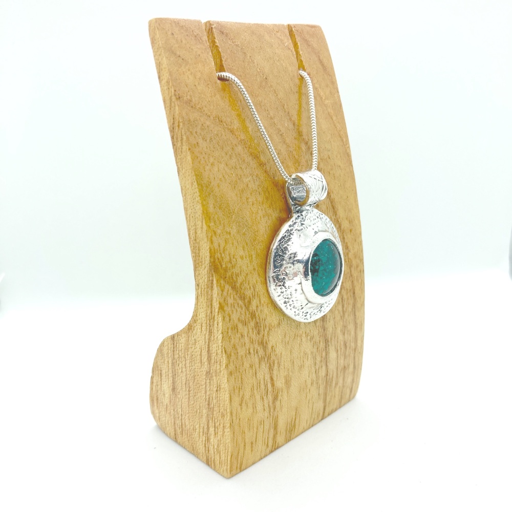 Solid silver handmade pendant with a circular design featuring a beautiful peacock green dichroic glass cabochon