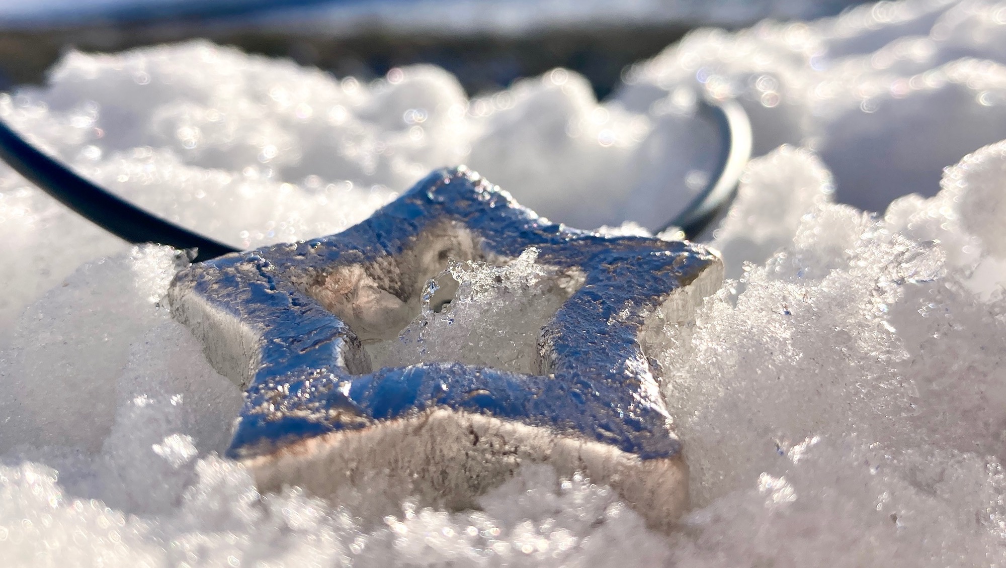 Silver Star Pendant in the snow, shown on rubber necklet
