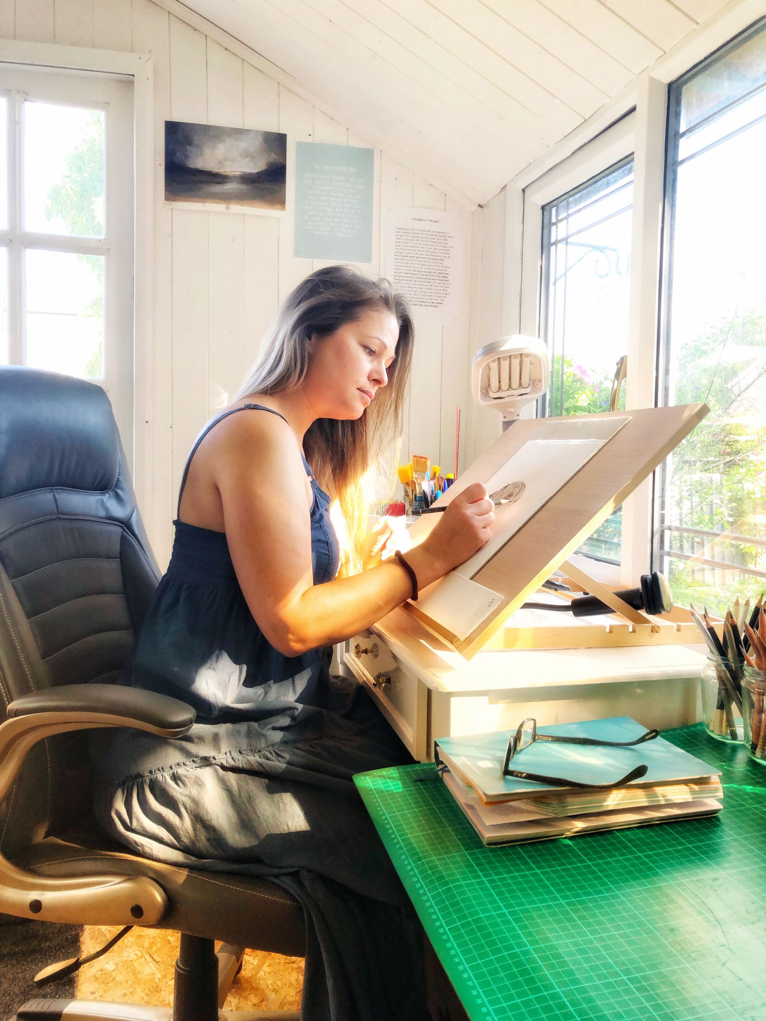 Carly drawing in her studio at the easel on the desk