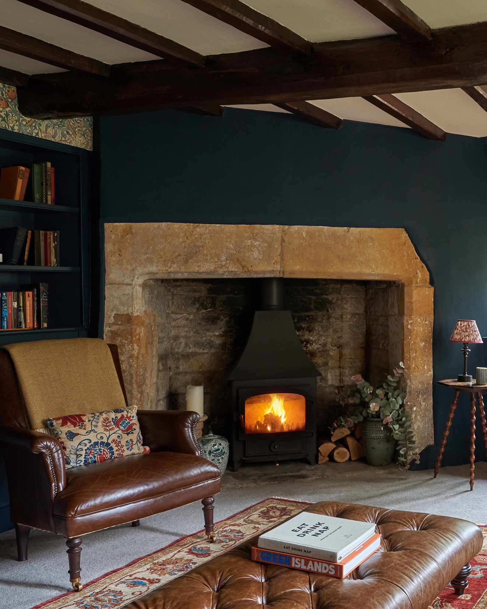 Hague blue farrow and ball snug with William Morris wallpaper, open stone fireplace with antique leather armchair and leather footstool