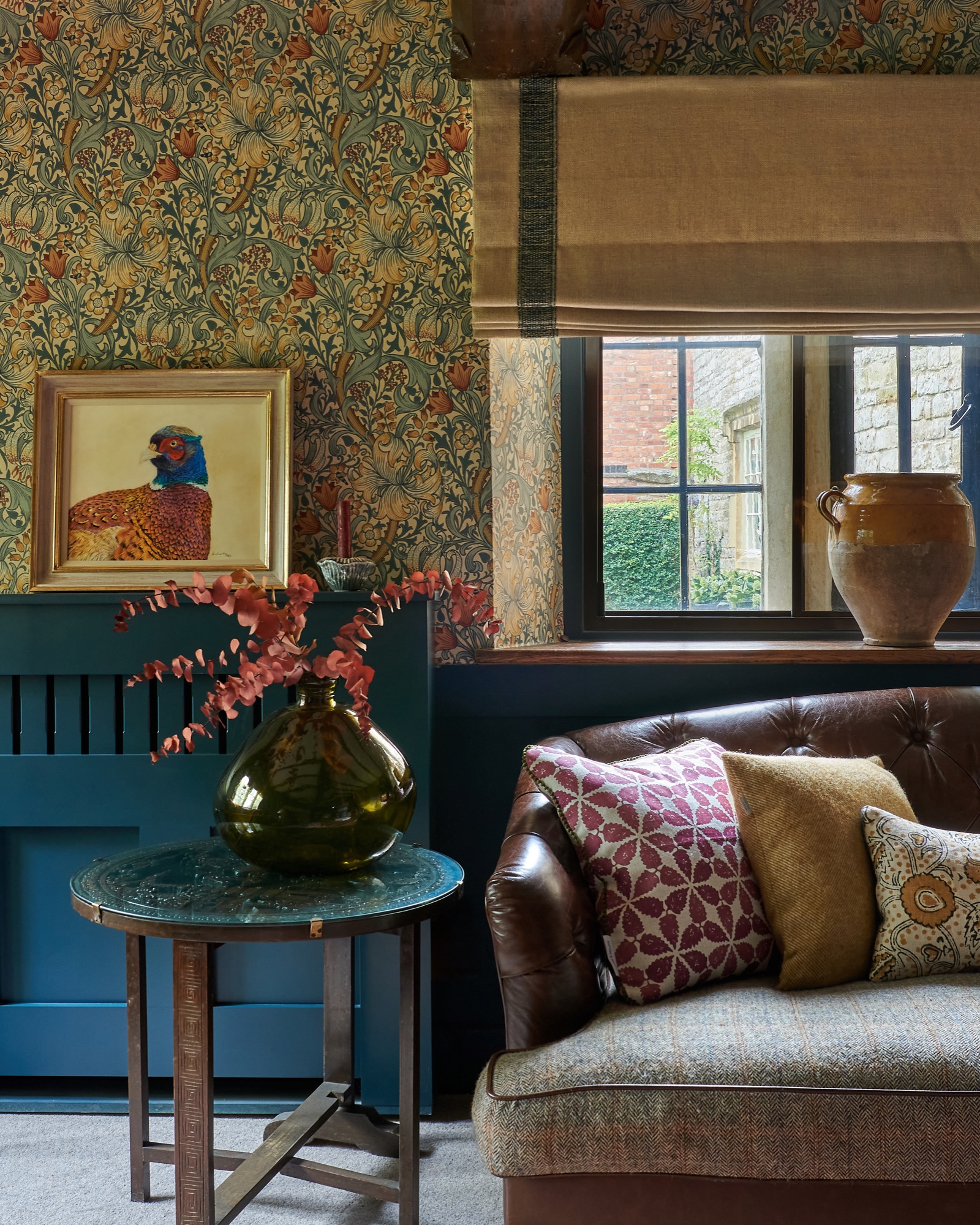 farrow and ball Hague blue snug with William Morris wallpaper, pheasant artwork, Ian main blinds with Samuel and sons trim, tetrad leather sofa with rapture and wright cushions, Linwood cushions, interior styling