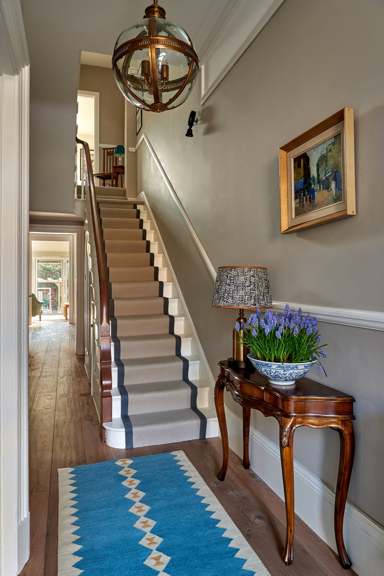 Light an airy hallway in a Georgian town house  painted in elephants breath farrow and ball with Beswick engineered oak flooring and a Sophie Cooney runner, antique console, Oka lamp and arti one vintage art.