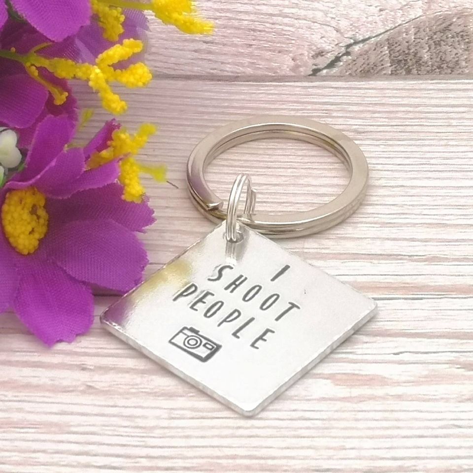 Square metal keyring with the wording, I shoot people & a small camera