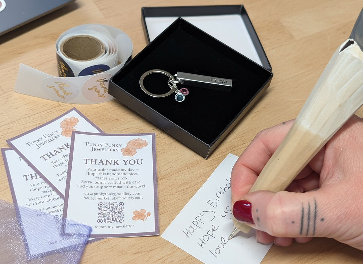 Handmade keyring in a gift box with birthstones and a handwritten gift note, shown on a warm, natural workspace with packaging details and thank-you slips.