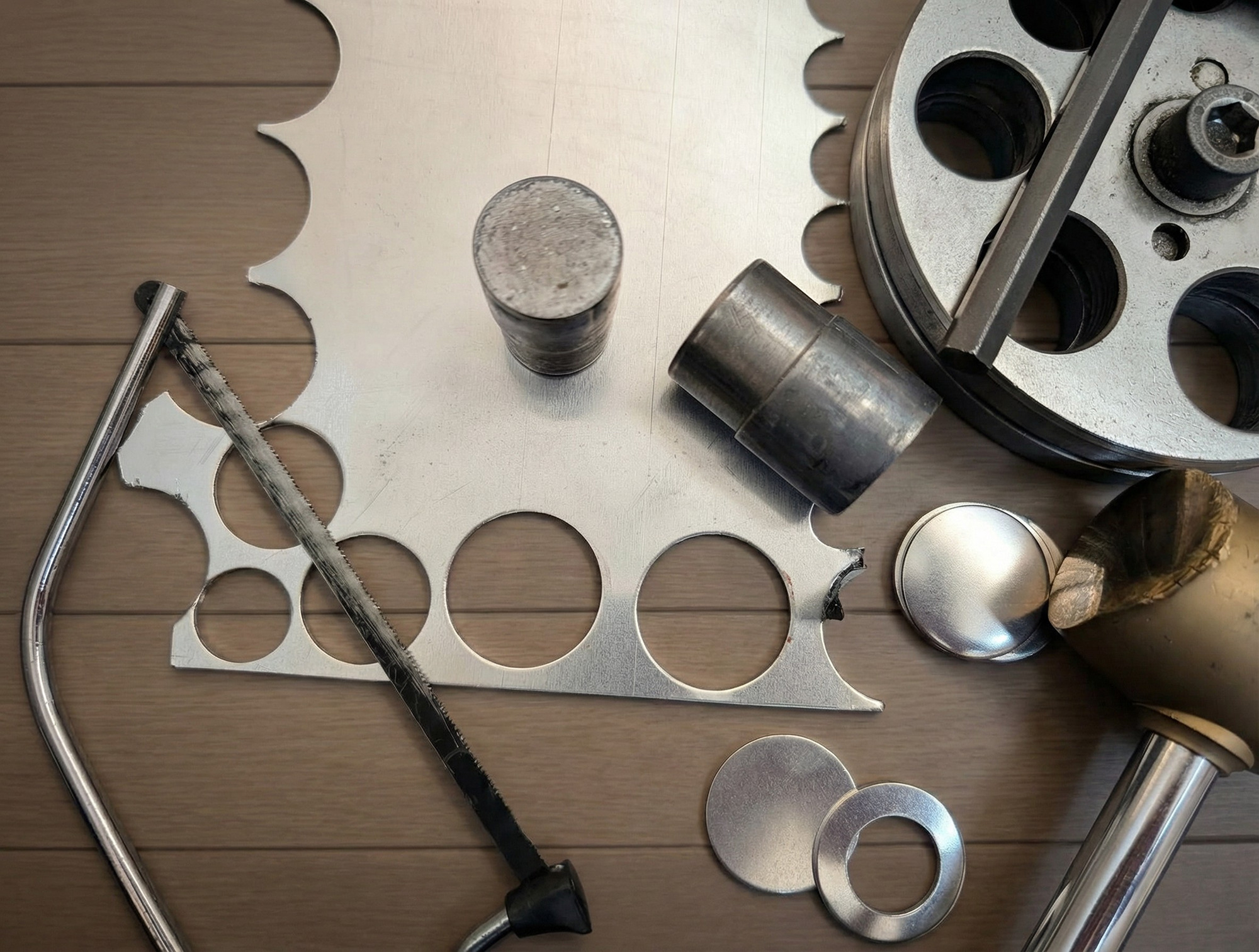 A close-up view of aluminium sheet metal with metal dies, hammer, cutter and freshly cut keyring blanks, showing the early stages of handmade stamping.