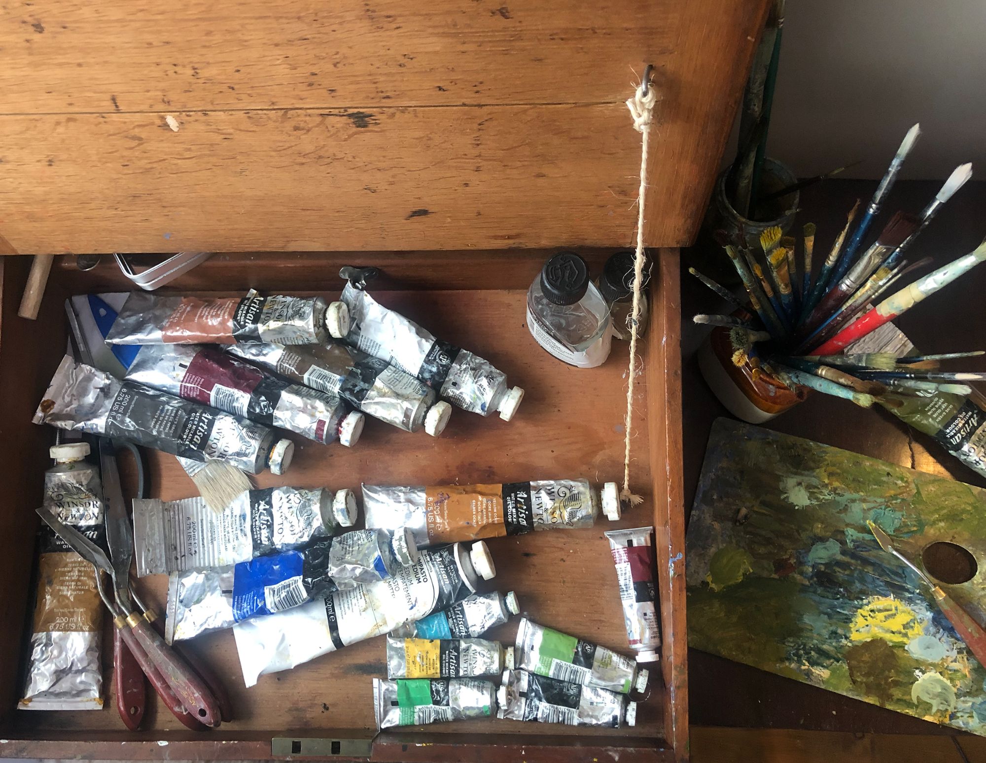 open drawer of paint tubes and brishes in a jar beside it. 